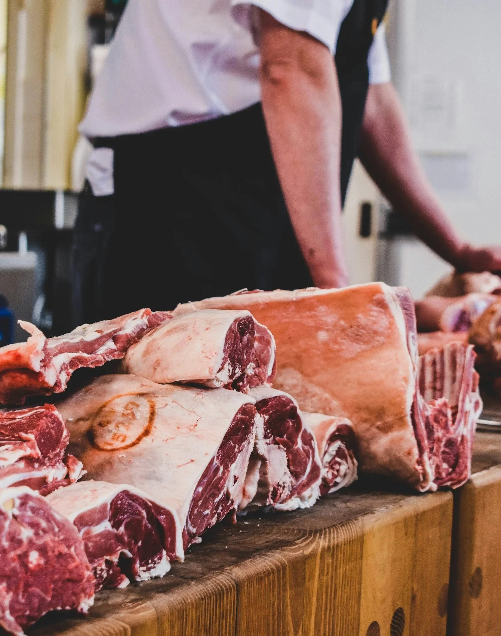 Raw large cuts of beef on a wooden counter with a butcher in the background.