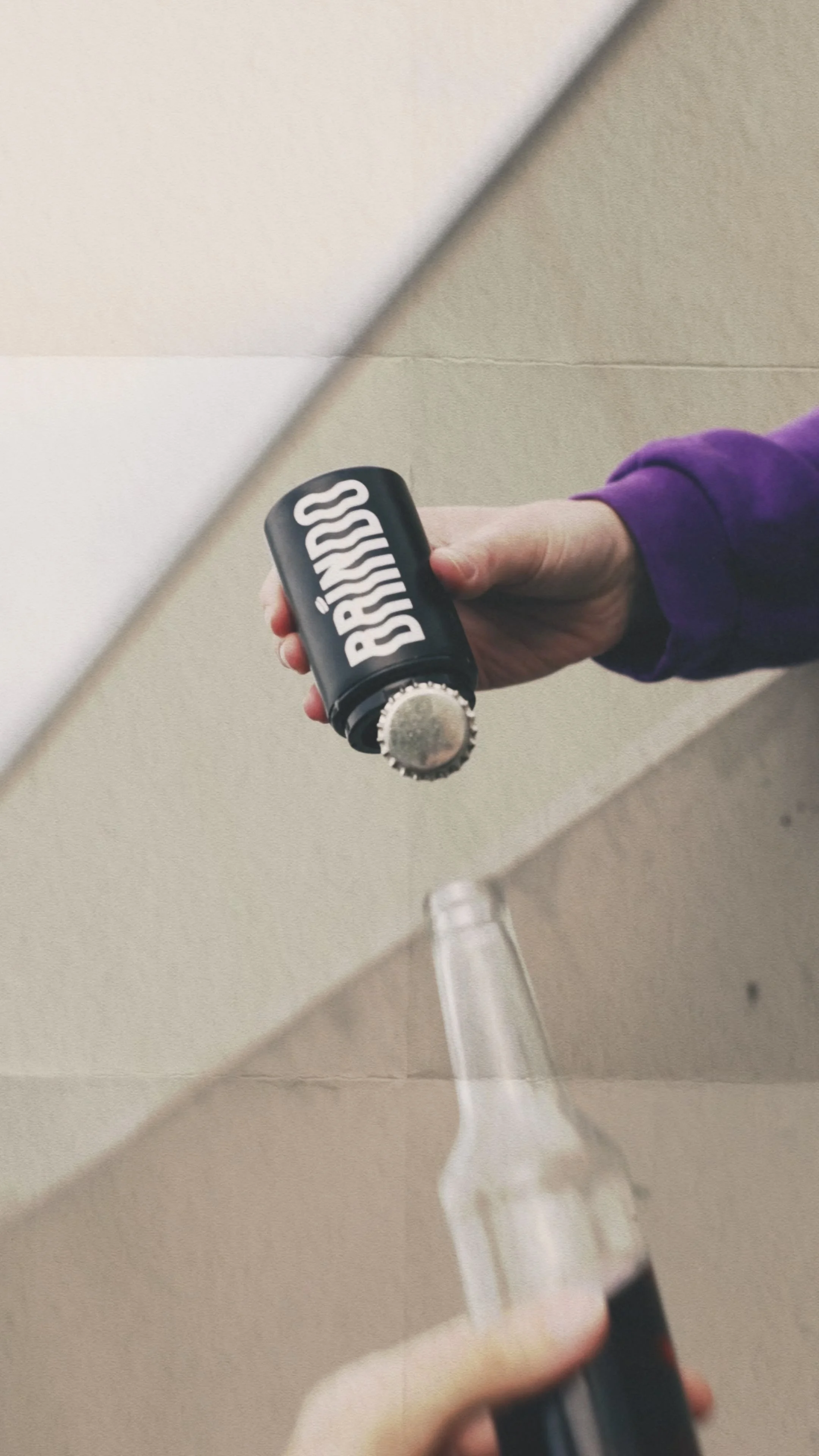 Una mano tiene una batteria di una bevanda energetica e sta versando in un bicchiere di vetro. Sullo sfondo, un muro beige e il pavimento in legno.