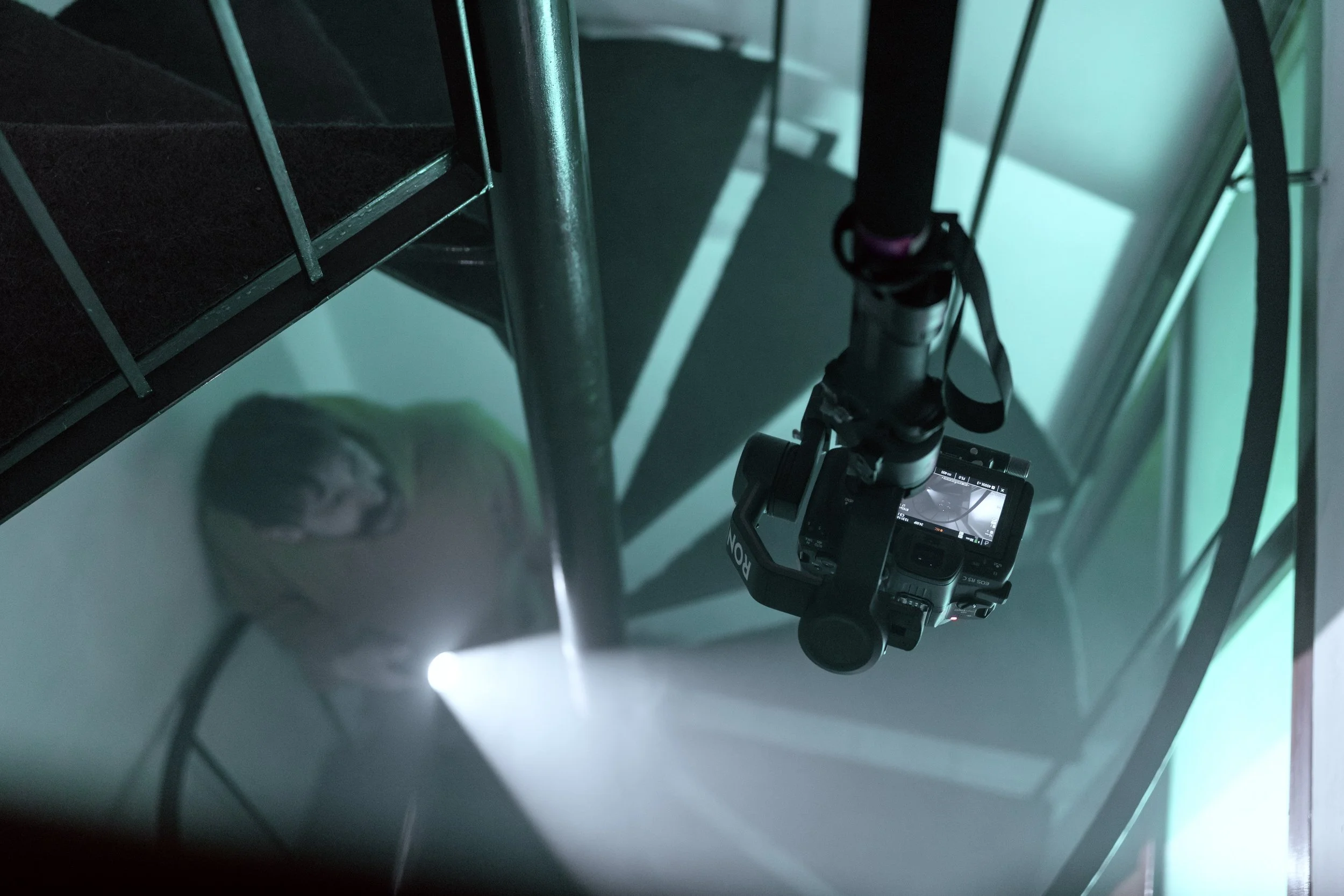 Fotografia di una fotocamera reflex digitale posizionata su una superficie bianca con una visuale dall'alto, circondata da scaffali metallici verdi in un ambiente ben illuminato.