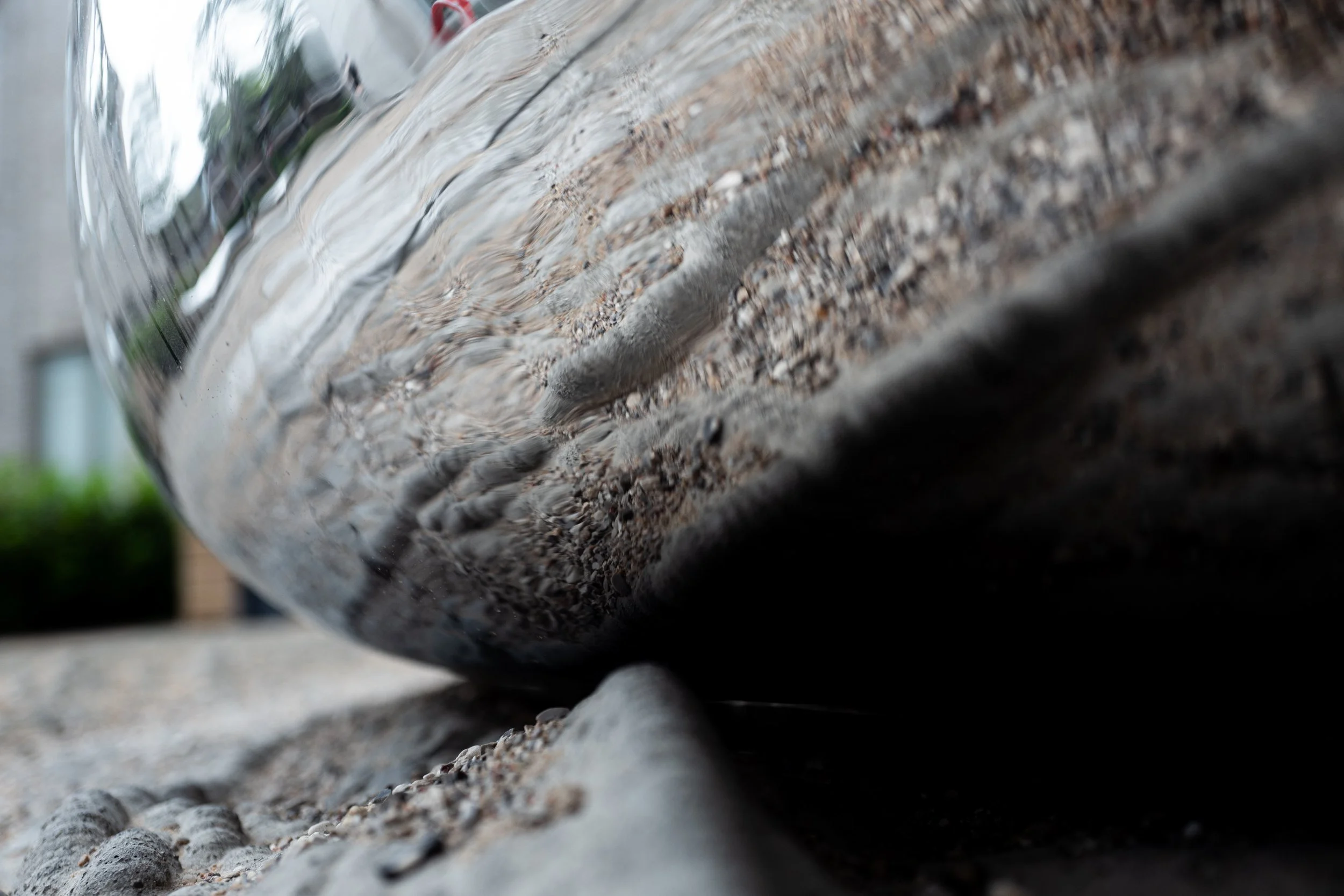 Nærbillede af en glaskugle, der ligger på en grusbelagt overflade, med reflektion af omgivelserne i glasset.