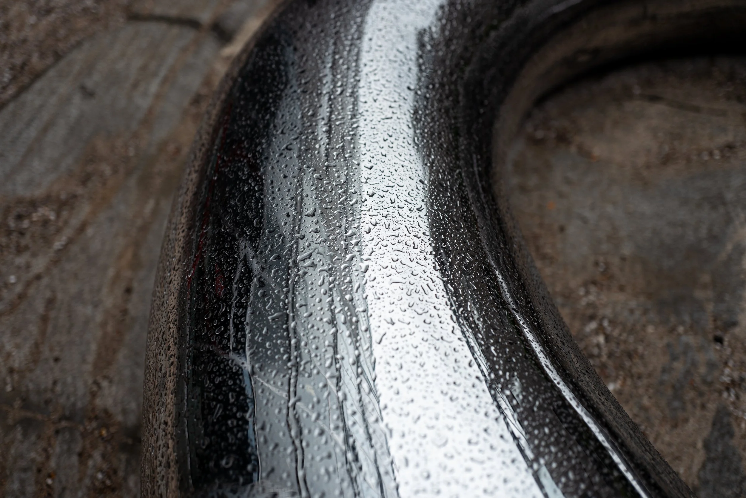 Nærbillede af en våd cykelramme, med raindråber på overfladen, omgivet af jord.