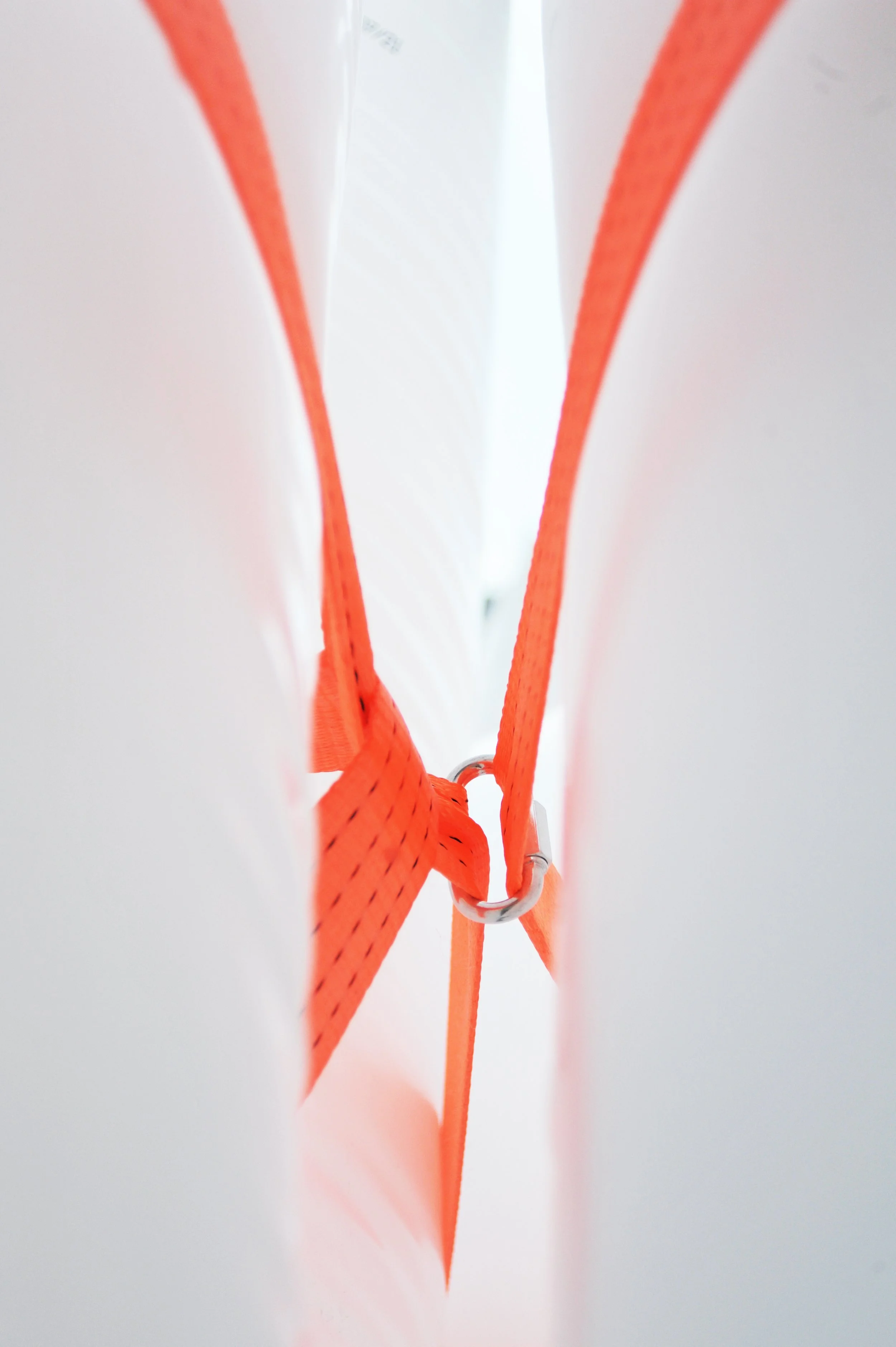 Nærbillede af to orange reb og en metalring, der holdes sammen af metalstifter, sat i mellem to hvide overflader.