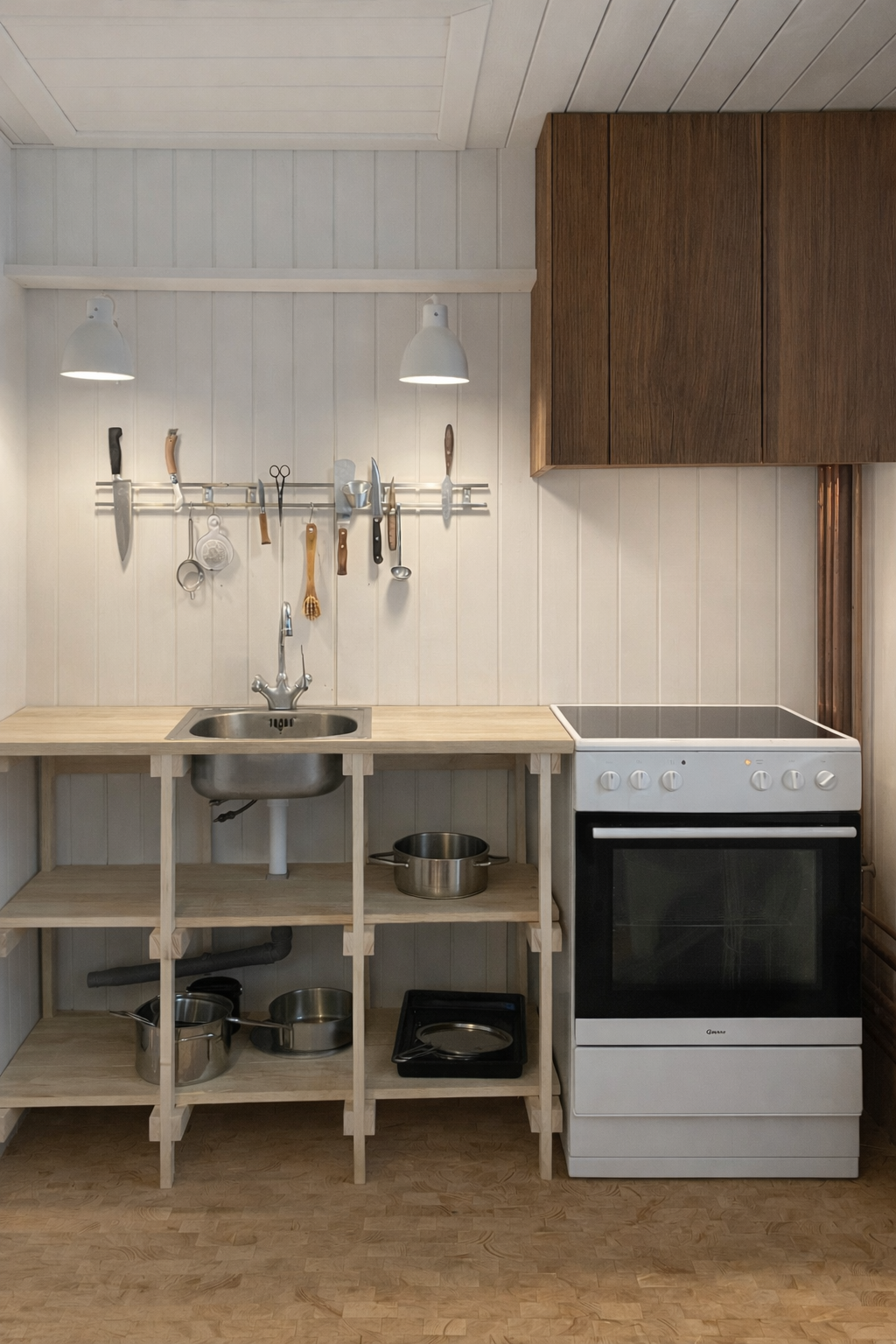 Køkken med åbent hyldesystem, vask, komfur, og nedenunder opbevaringshylder, oplyst af to væglamper.