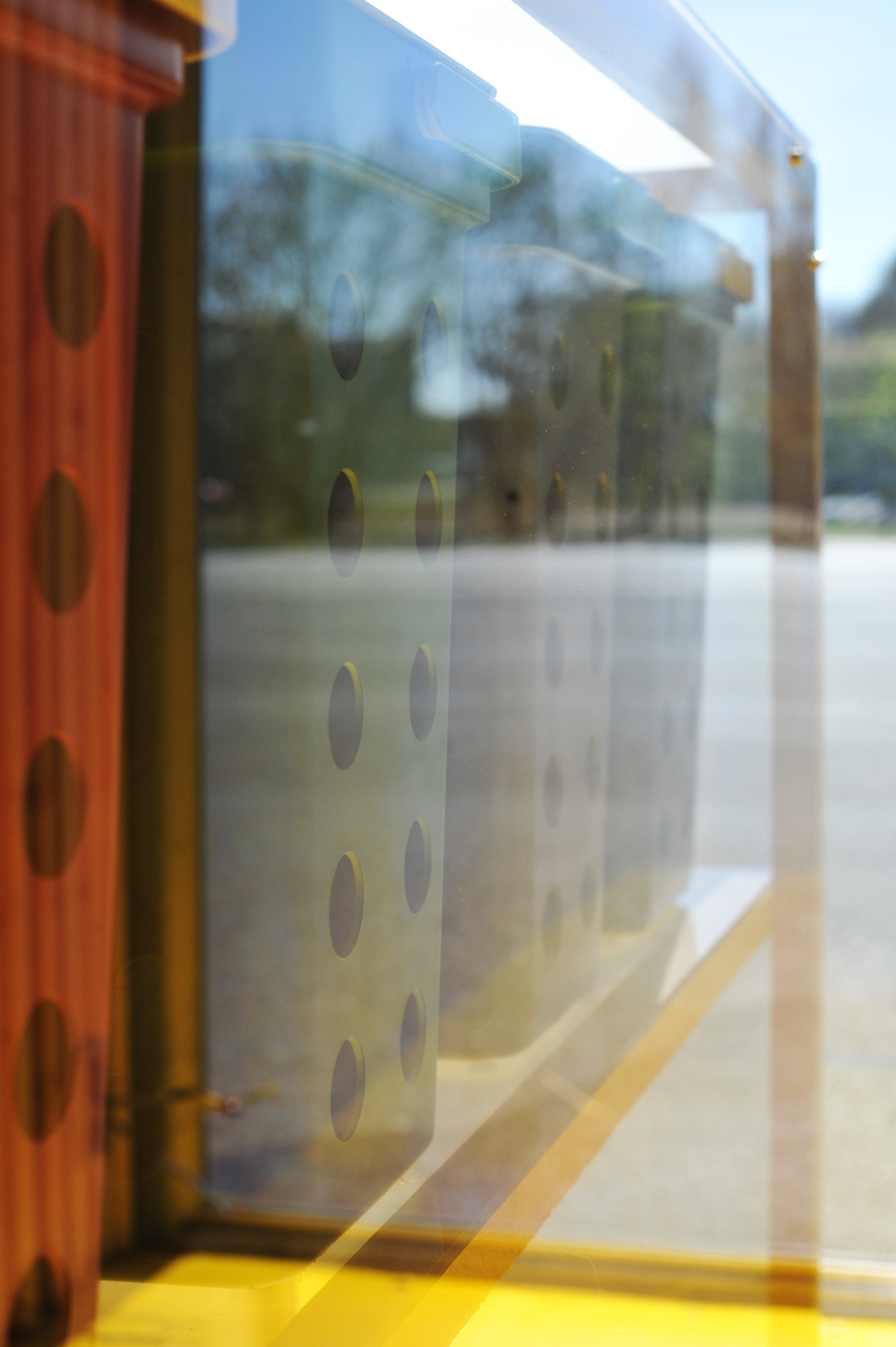 En vindueskarm med en metalplade med cirkulære huller, set fra indersiden, med en udendørs scene i baggrunden.