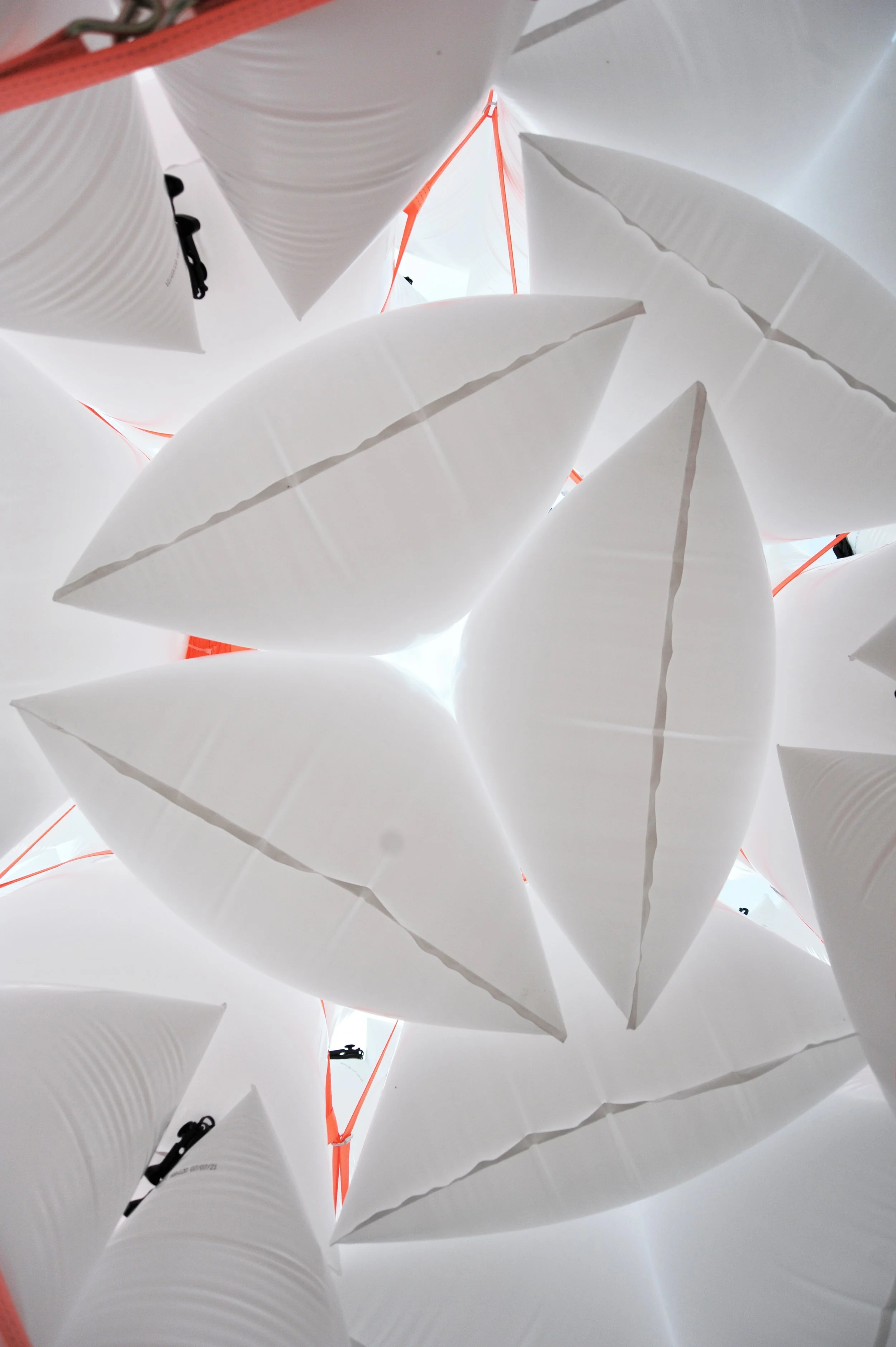 Hvide, oppustelige, trekantede lysarmaturer set udefra, med nogle røde stropper og sorte elasticitetssnore.