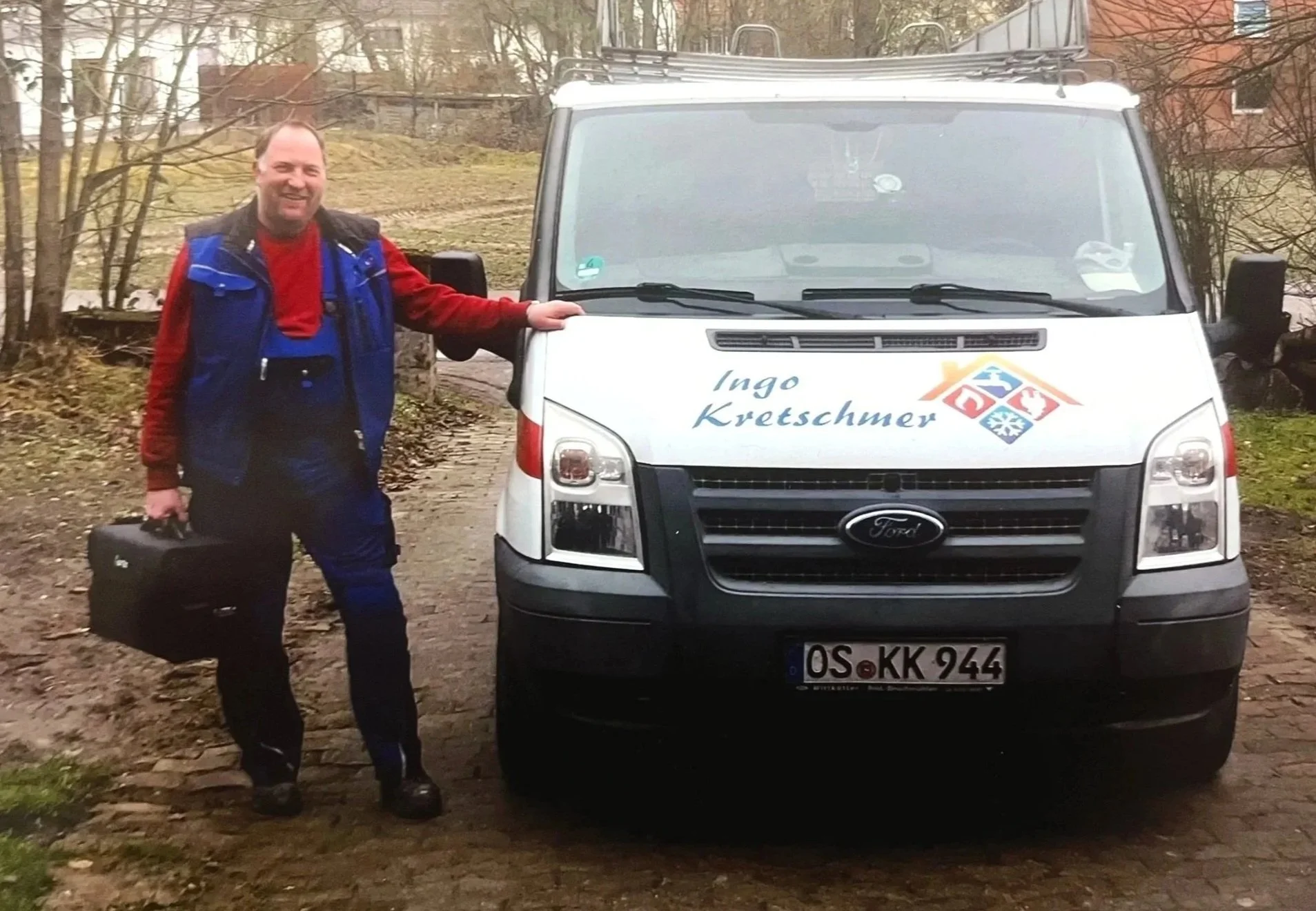 Ingo Kretschmer steht neben einem weißen Ford Transit mit dem Schriftzug 'Ingo Kretschmer' auf der Motorhaube, hält eine schwarze Tragetasche in der Hand und trägt Arbeitskleidung.