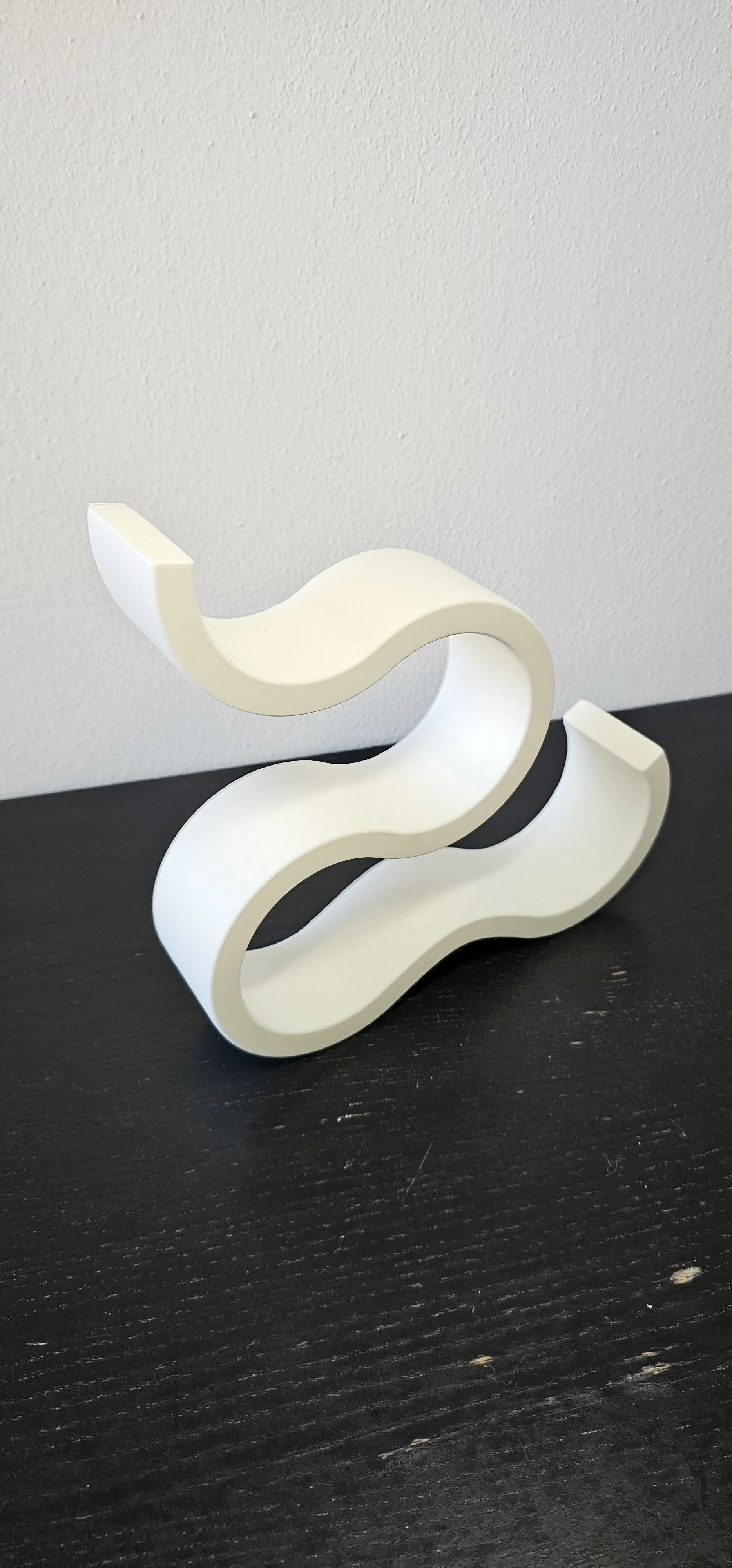 Scultura decorativa bianca porta vino con forma curvilinea su superficie scura.