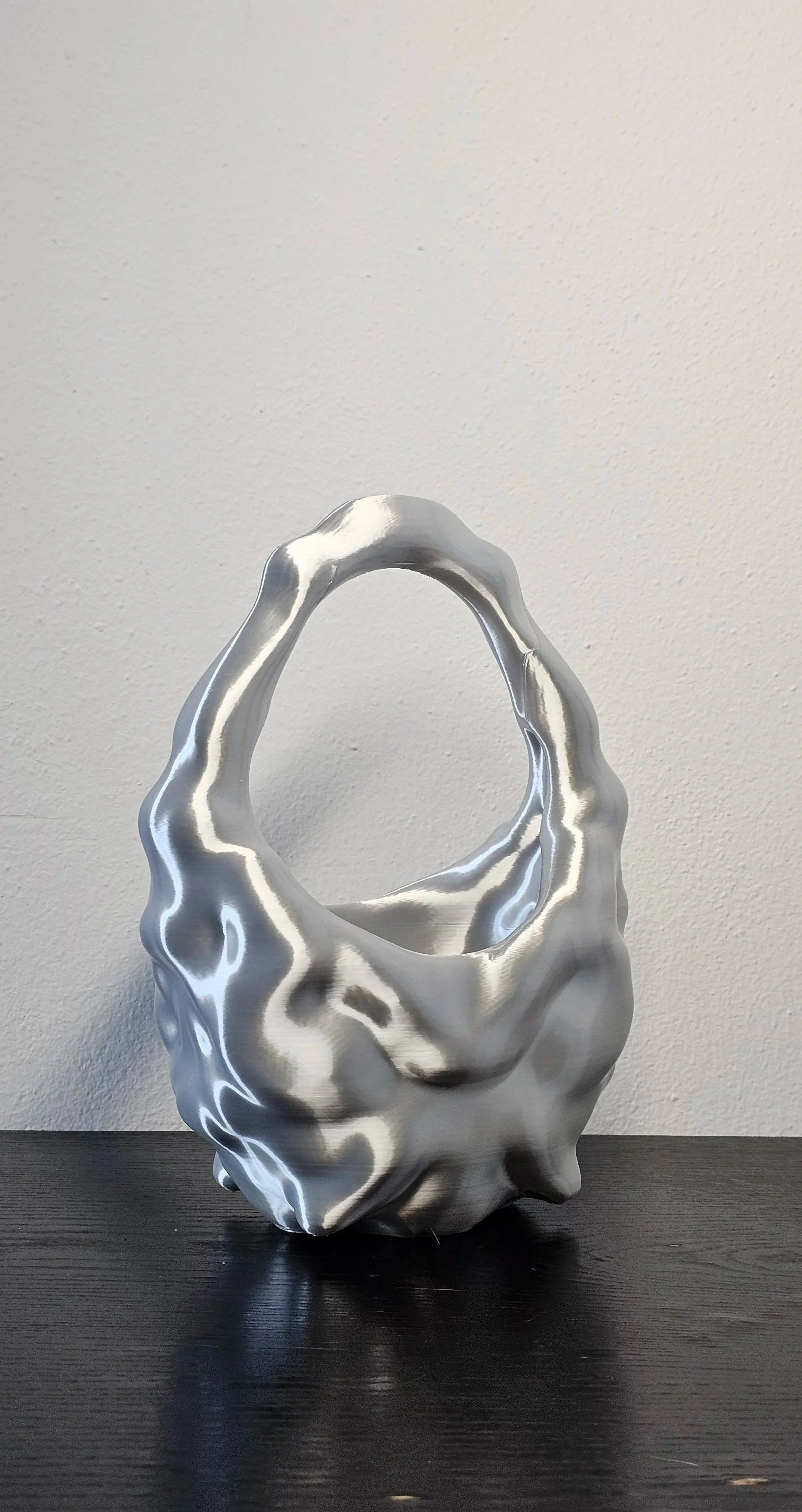 Scultura moderna in metallo argentato a forma di borsa, posizionata su un tavolo nero.