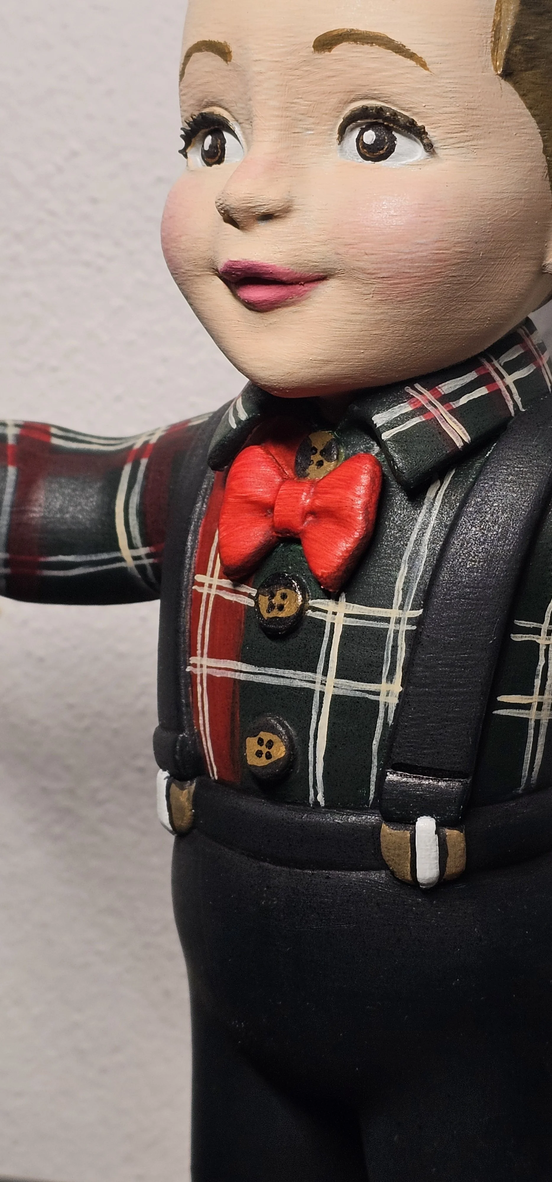 Statua di un bambino con pantaloni neri, camicia a quadri e papillon rosso.