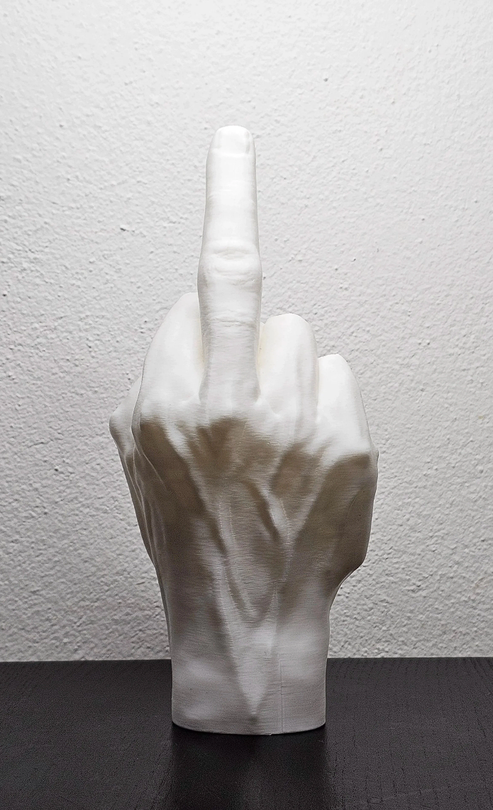 Statua di una mano con il dito medio alzato, di colore bianco, posizionata contro una parete bianca e su una superficie nera.
