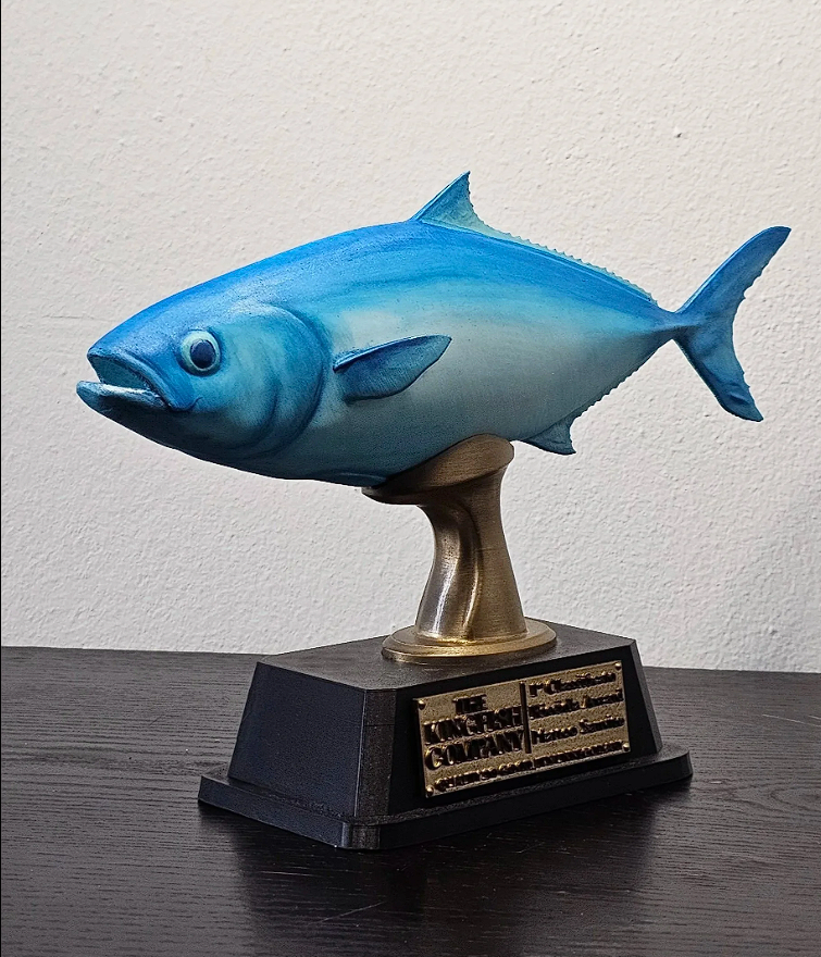 Trofeo di una pesciola blu con grande bocca, montato su una base nera con placca dorata.