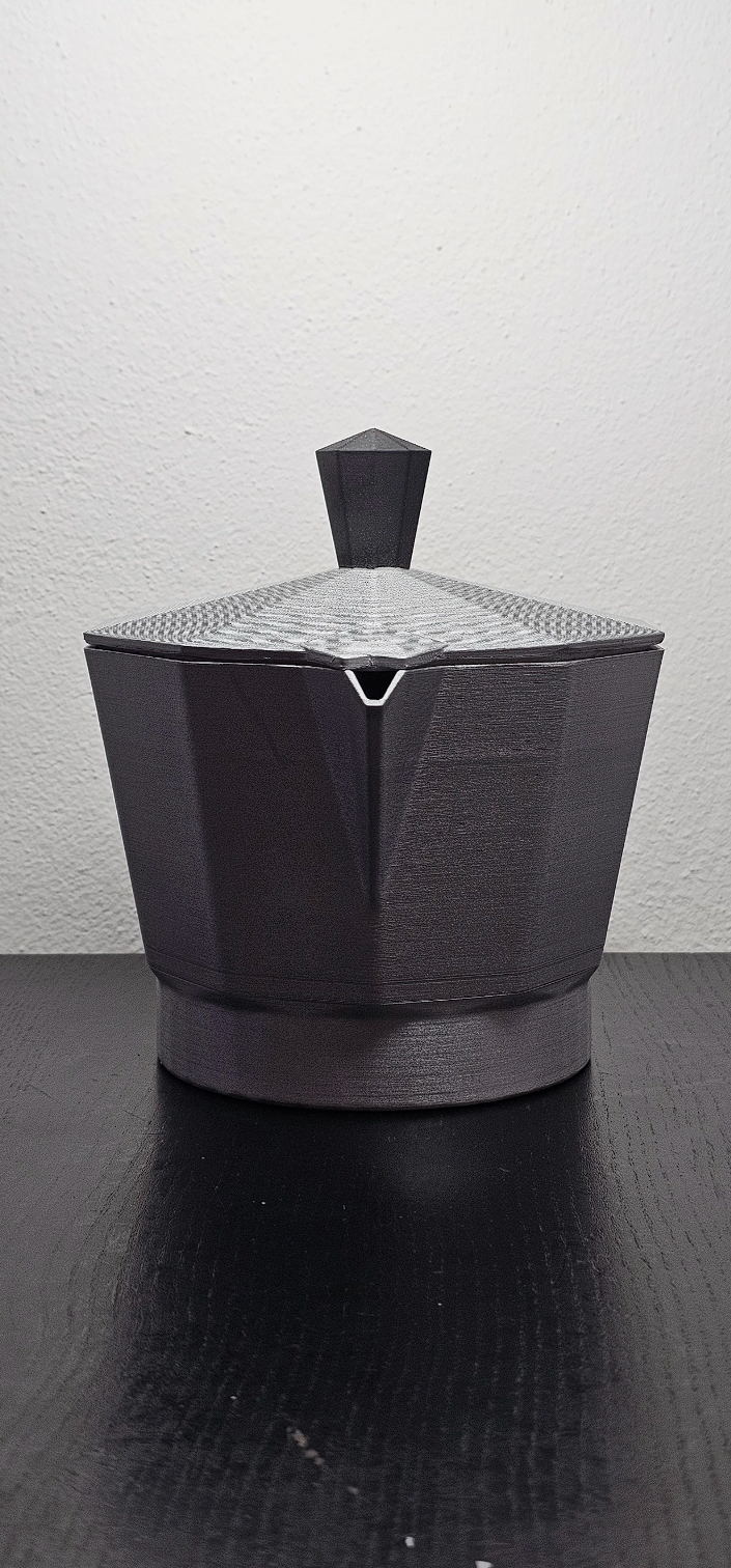 Sorpresore di forma quadrata e nera con un coperchio a punta, posizionato su una superficie nera con sfondo bianco.