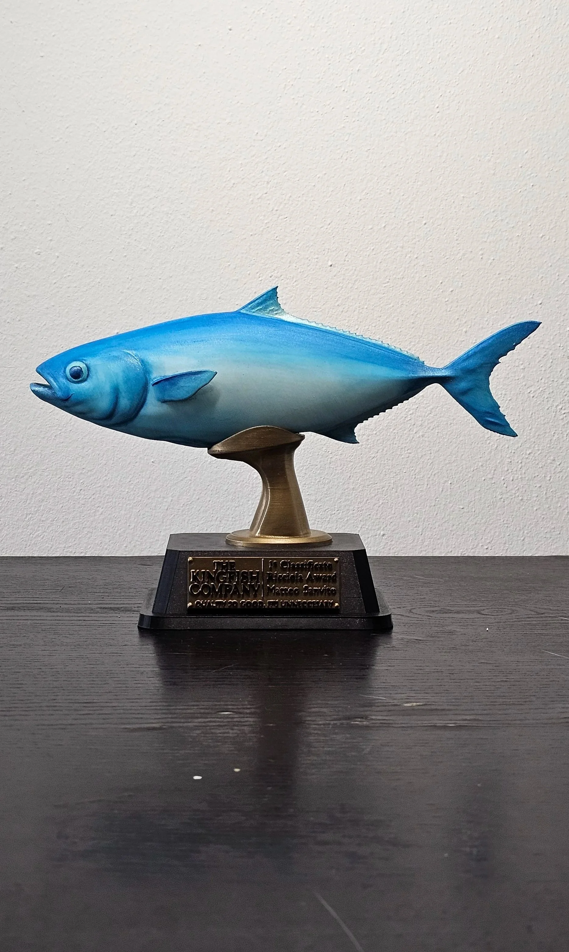 Trofeo a forma di pesce blu su base in legno con targhetta.