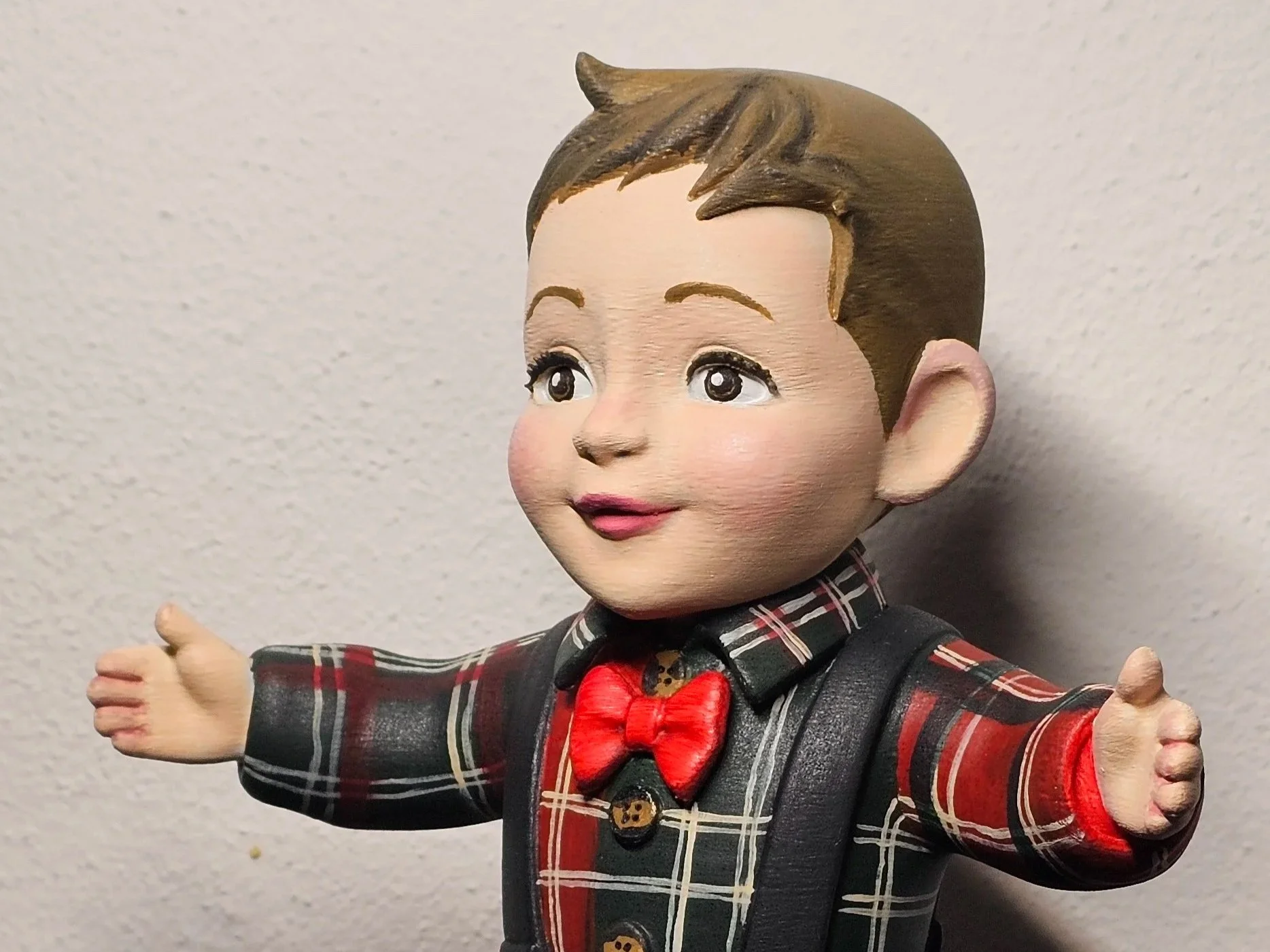 Statua dipinta a mano di un bambino in abiti con motivo scozzese e cravatta rossa, con le braccia aperte.