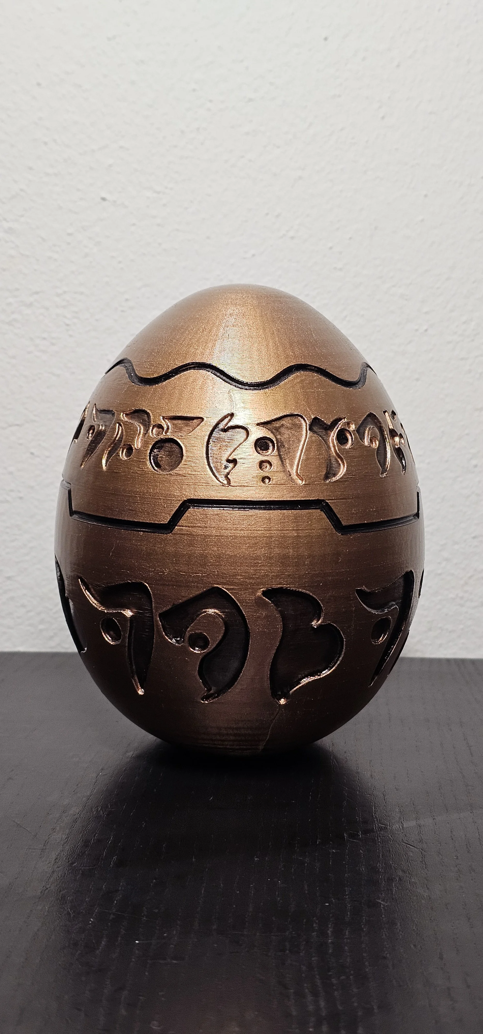 Uovo di cioccolato decorato con incisioni di simboli e disegni, di colore marrone scuro, posato su una superficie nera.