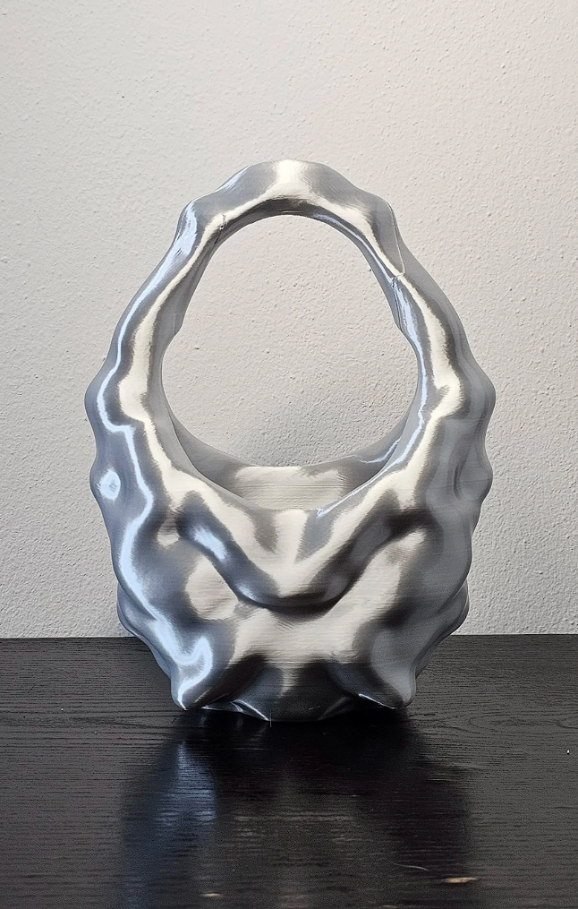 Scultura di metallo con forma organica e apertura centrale, posizionata su un tavolo nero