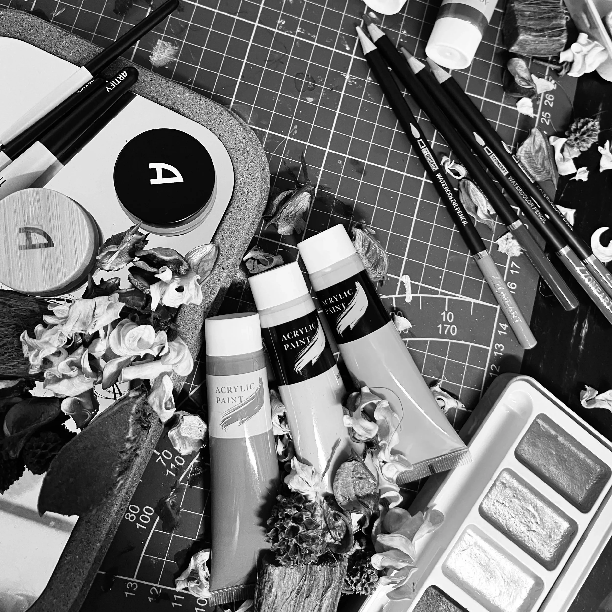 Tavolo da lavoro con colori acrilici, pennelli, palette, tubetti di acrilico, foglie secche e fiori secchi.