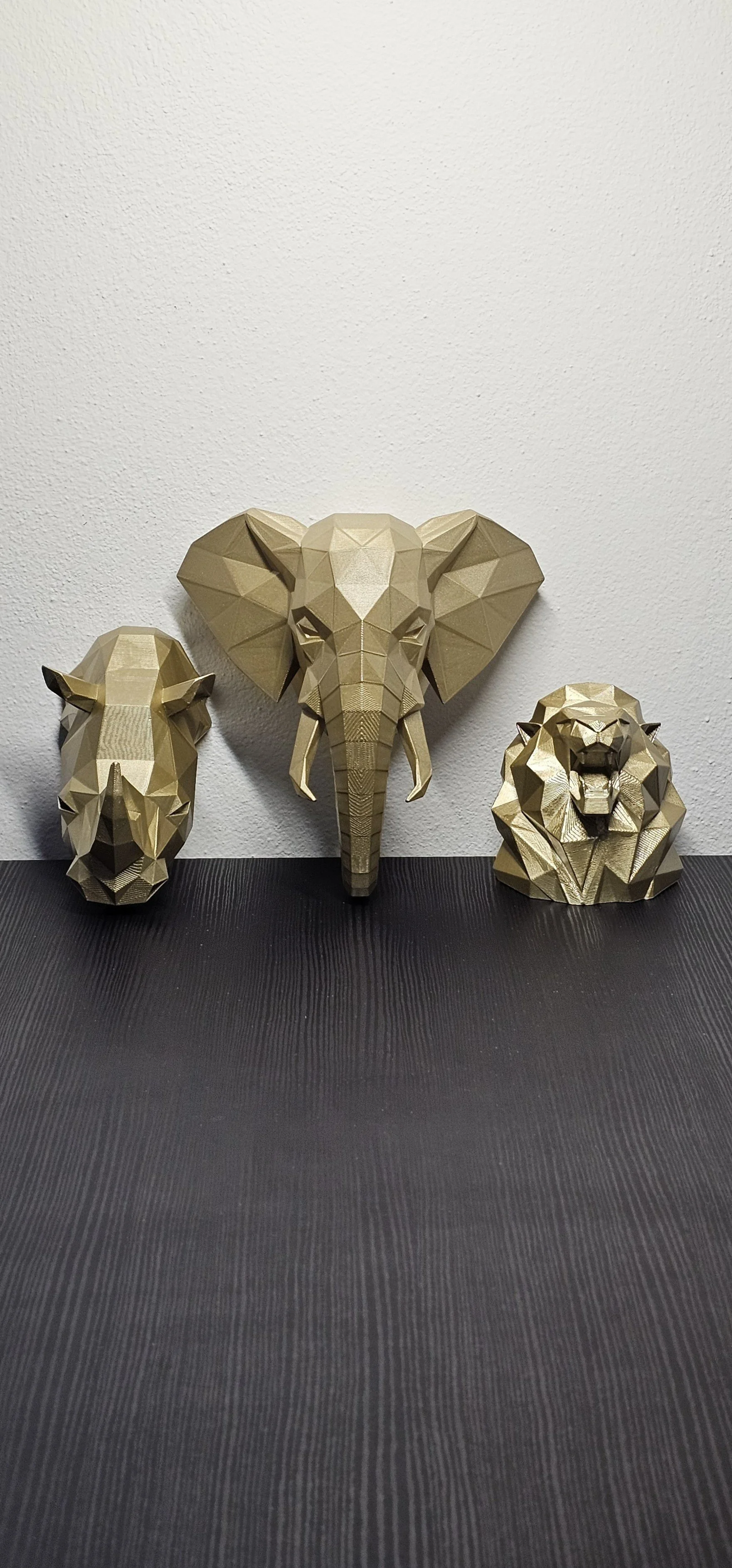 Sculture geometriche di un elefante, un leone e un bisonte in stile moderno, posizionate su un tavolo nero contro una parete bianca.