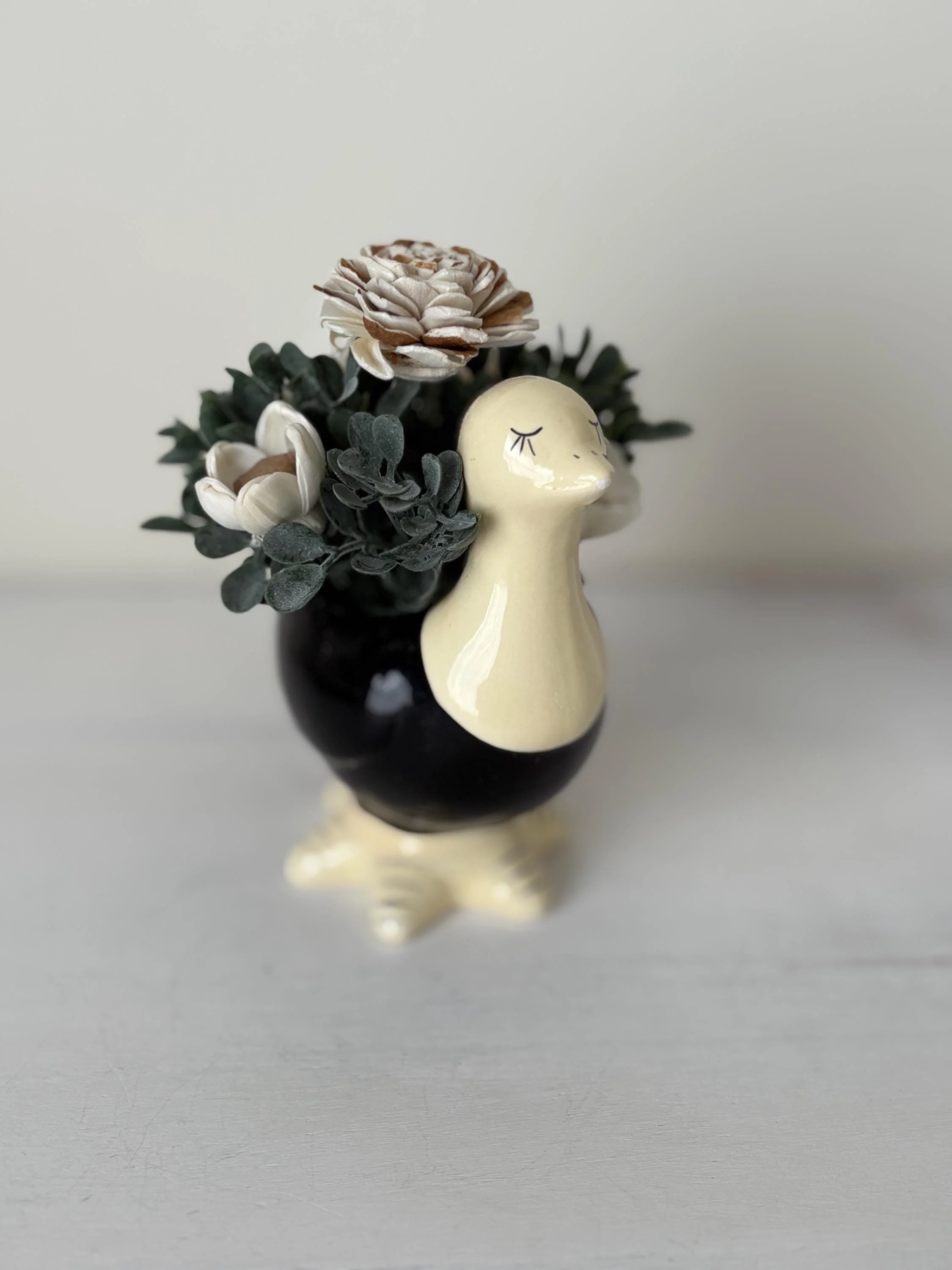 Ivory and cocoa-tipped sola wood flowers in a black and cream ceramic ostrich planter with a sleeping face.