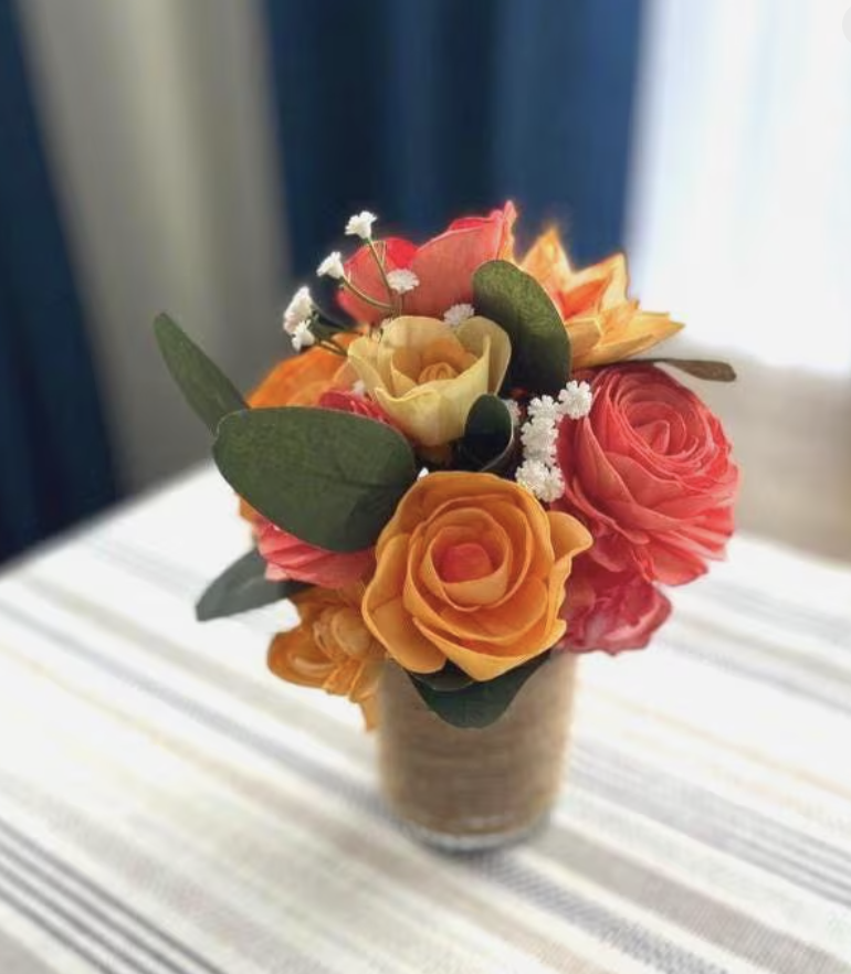 A small bouquet of artificial roses and other flowers in a glass vase on a striped tablecloth.