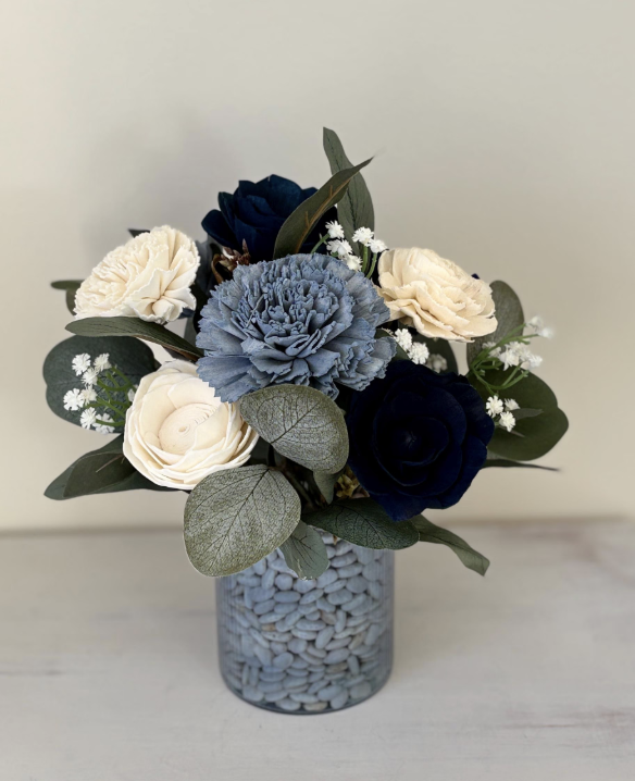 A bouquet of flowers in a glass vase containing blue and white flowers with green leaves and small white filler flowers.
