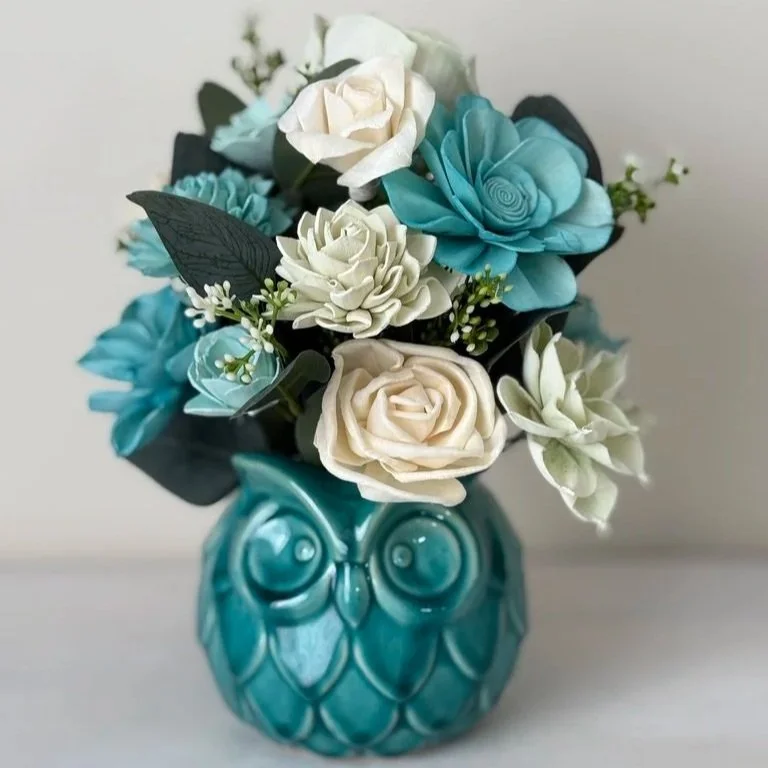 Decorative bouquet of artificial flowers in a turquoise owl-shaped vase.