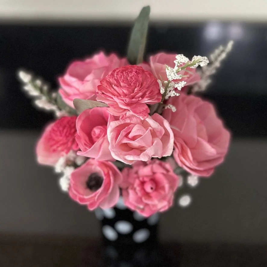 A bouquet of pink and red flowers in a black vase with white polka dots.