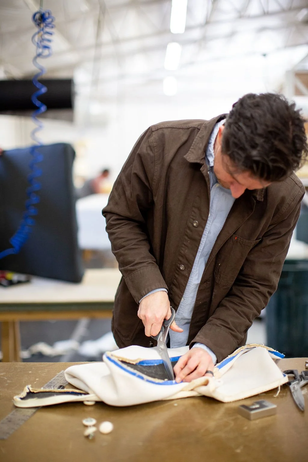 A man cutting fabric with scissors on a worktable in an upholstery workshop.