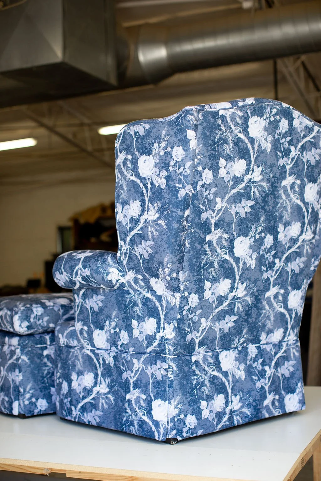 A blue floral upholstered armchair with white flower pattern in an industrial warehouse setting.