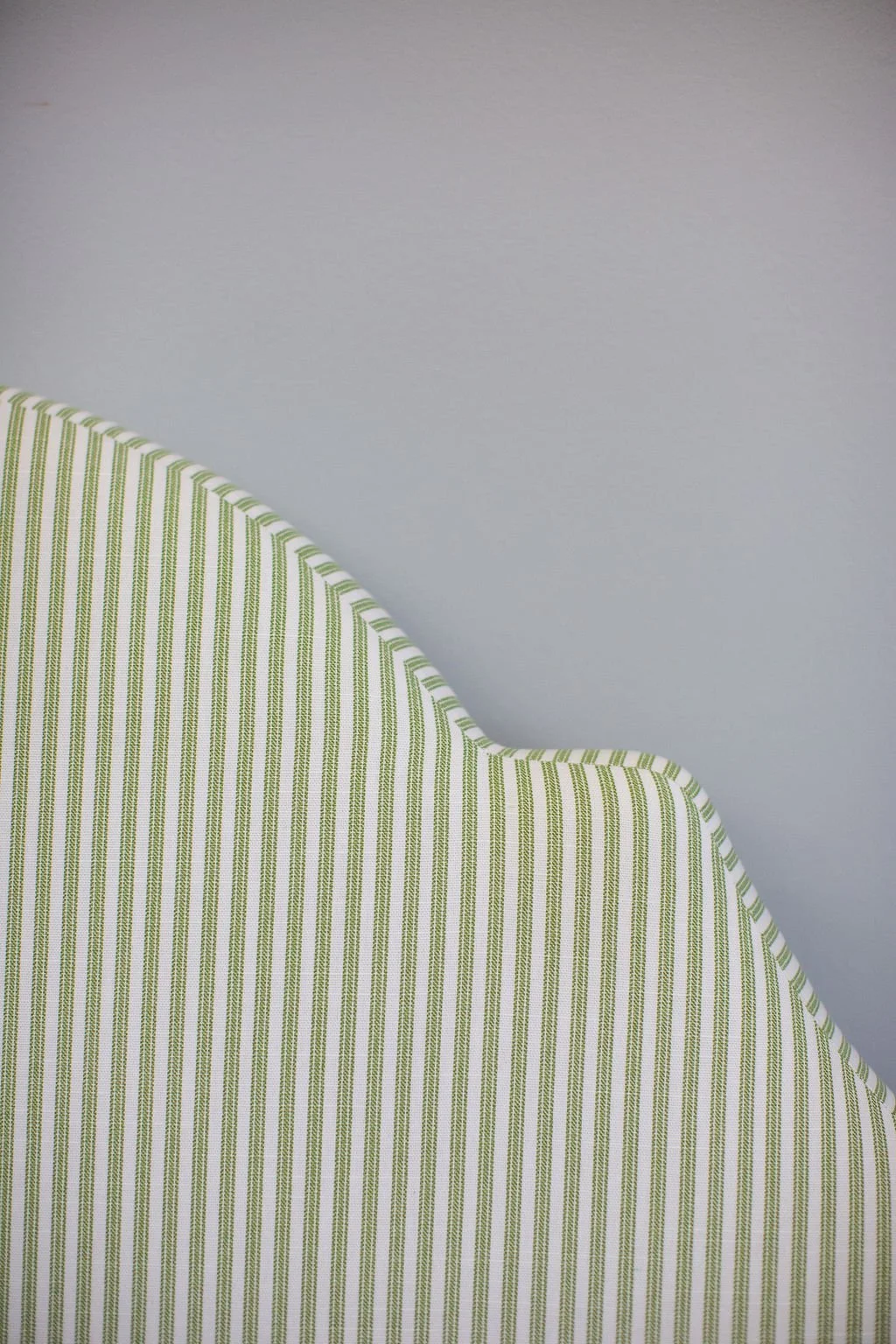 Close-up of a green and white striped upholstered headboard against a gray wall.