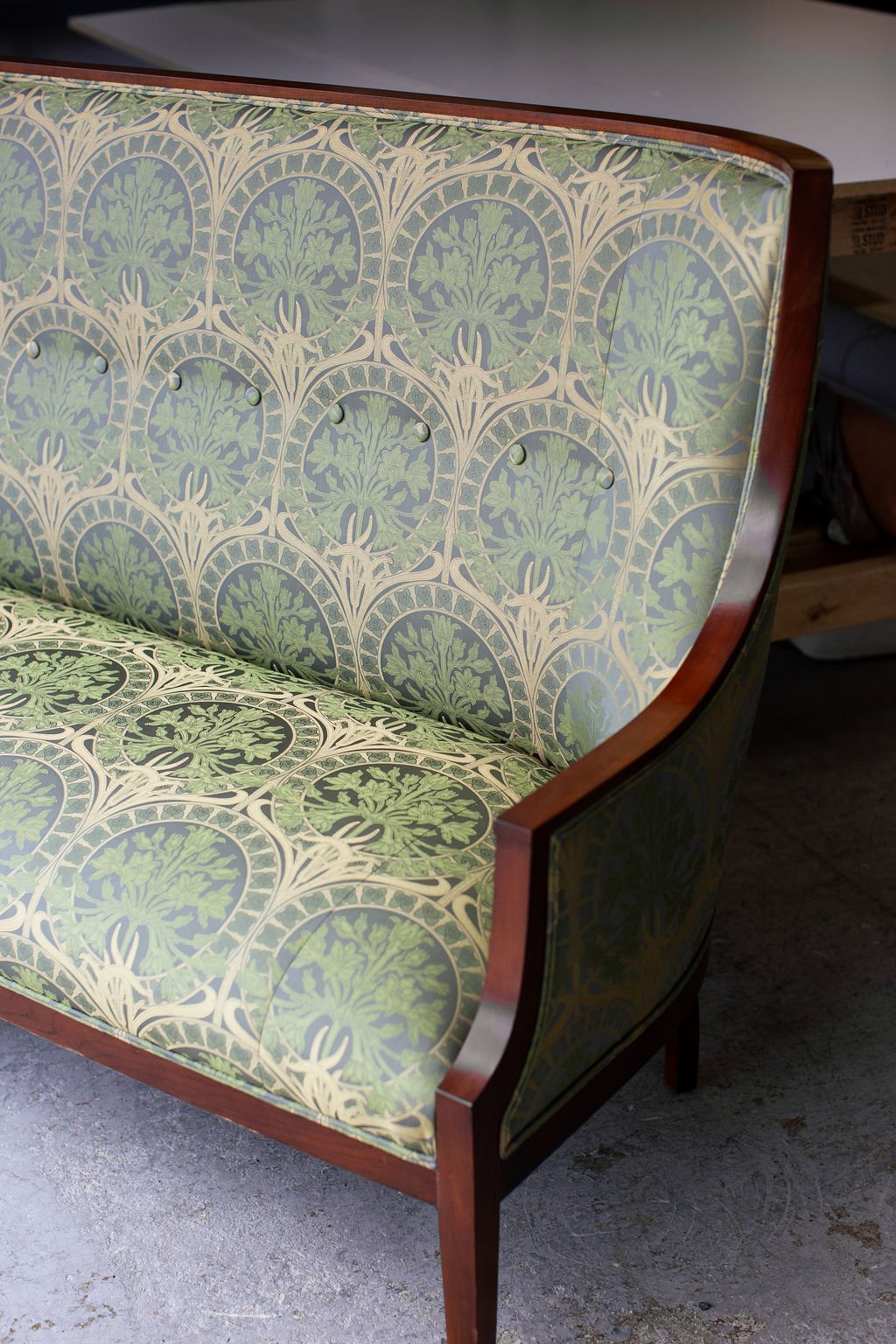 Close-up of vintage sofa with green and cream patterned upholstery and wooden frame.