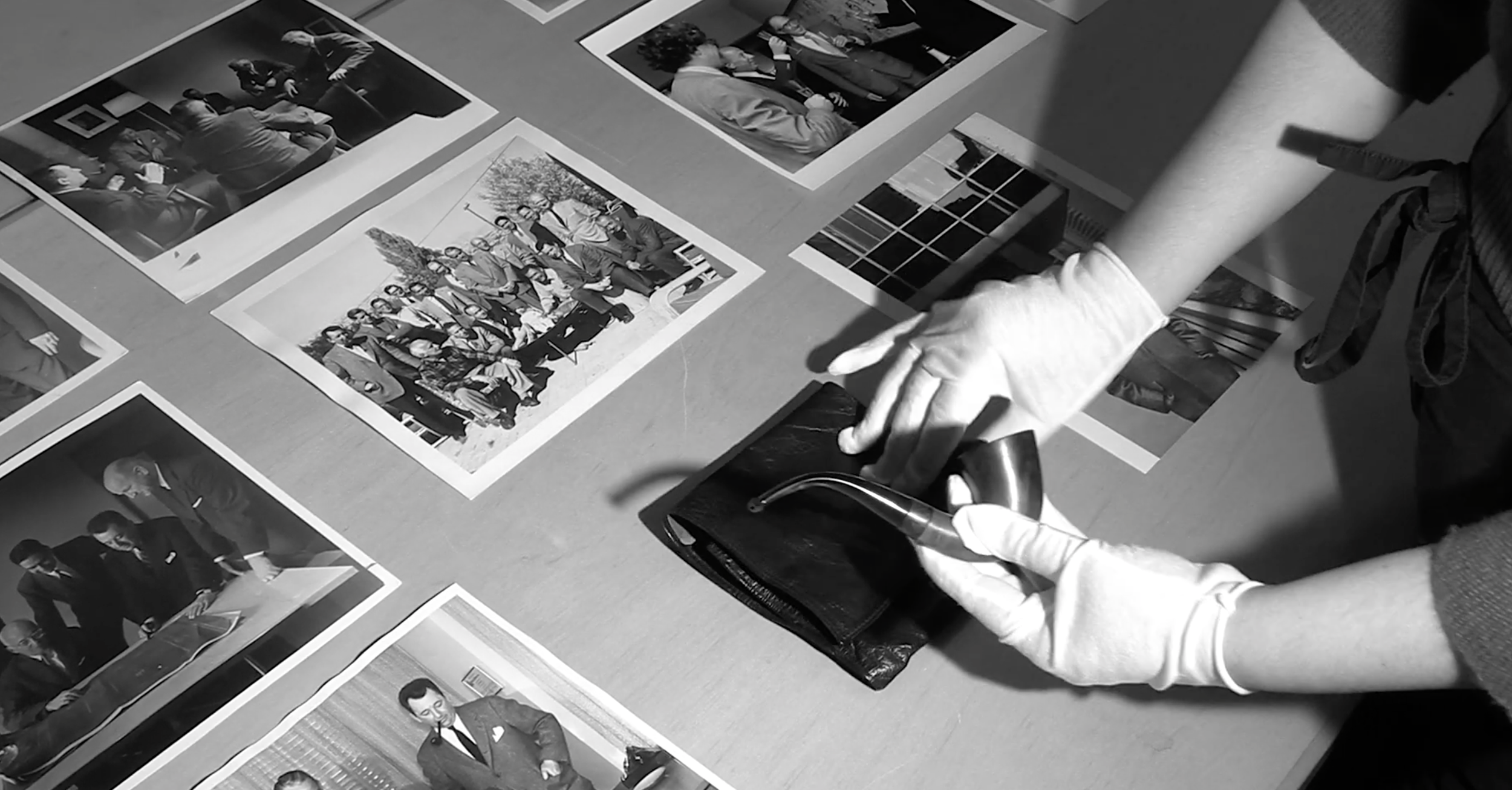 A person wearing gloves handling a pipe and a wallet on a table covered with printed photographs.