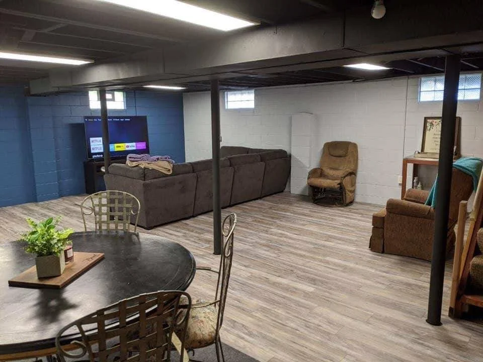 Basement living room with a large brown sectional sofa, an armchair, a TV, and a dining table with chairs.