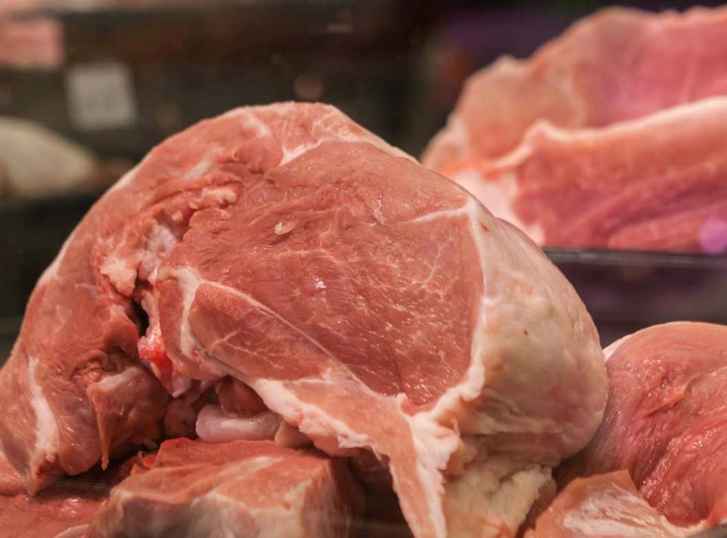Raw pork meat with some fat, on a dark surface.