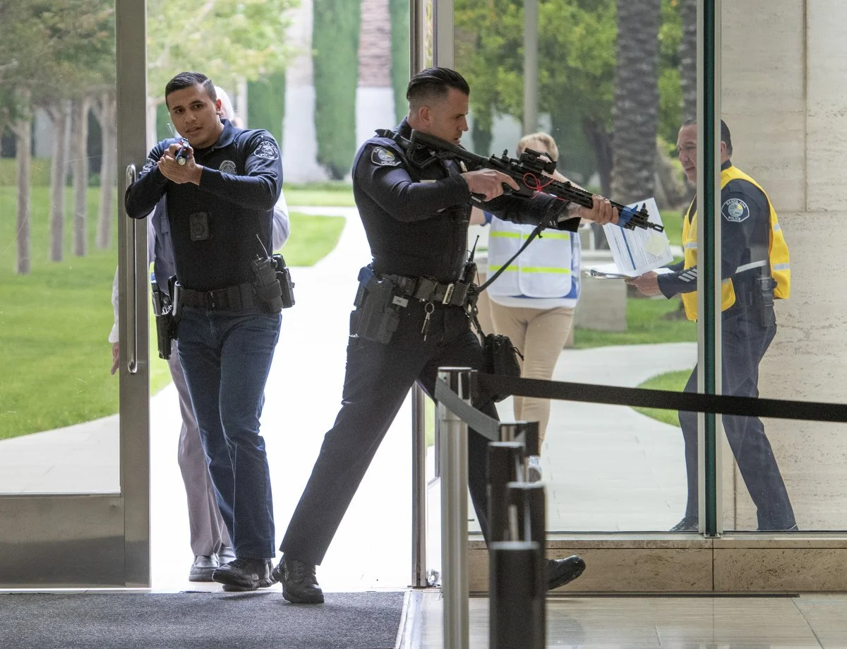 Police officers and a security guard engaging in a standoff or security operation inside a building near the entrance, with one officer aiming a rifle through a glass door.