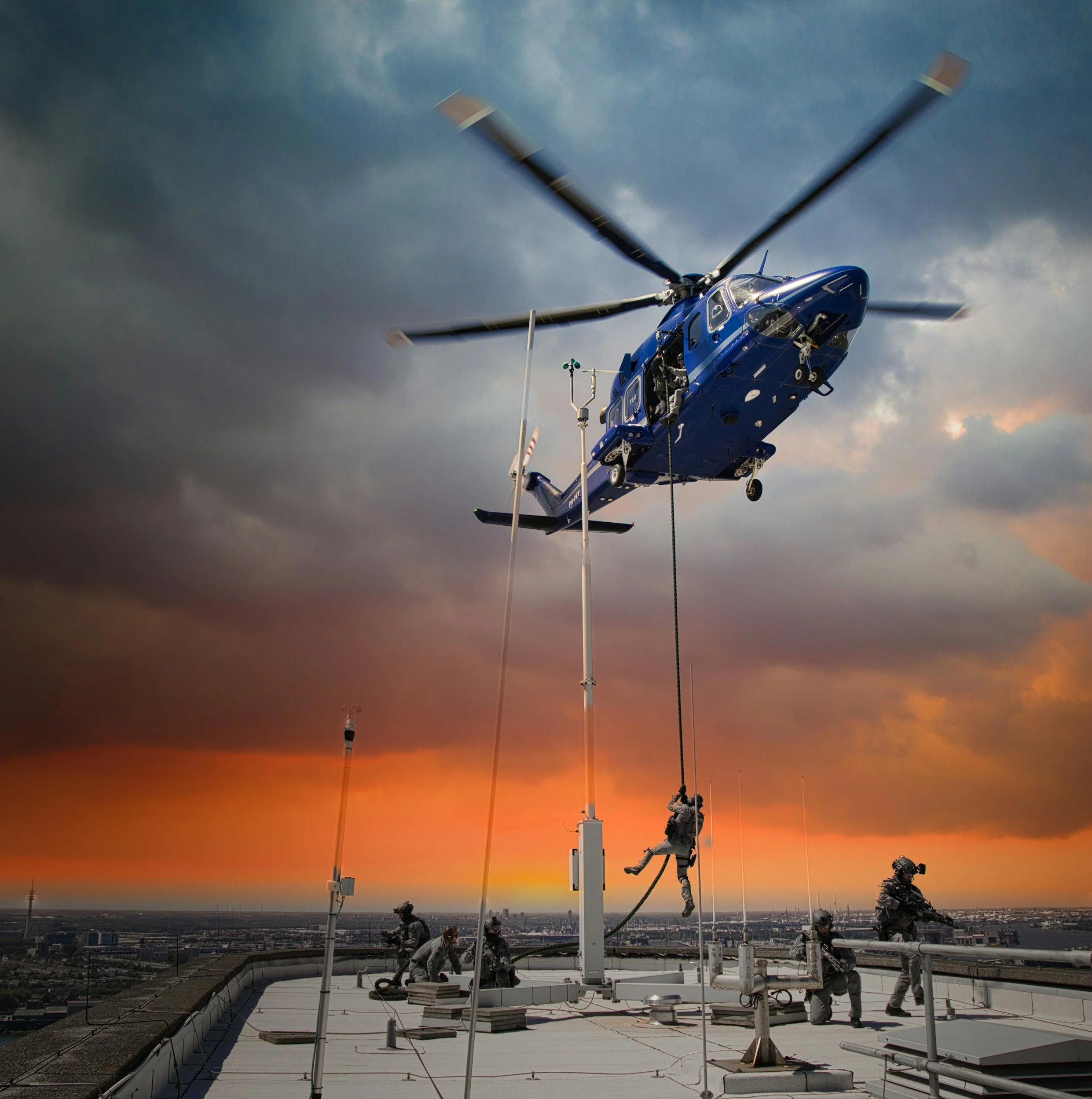 Military helicopter hovering above a rooftop with soldiers, one climbing a rope, against a sunset sky.