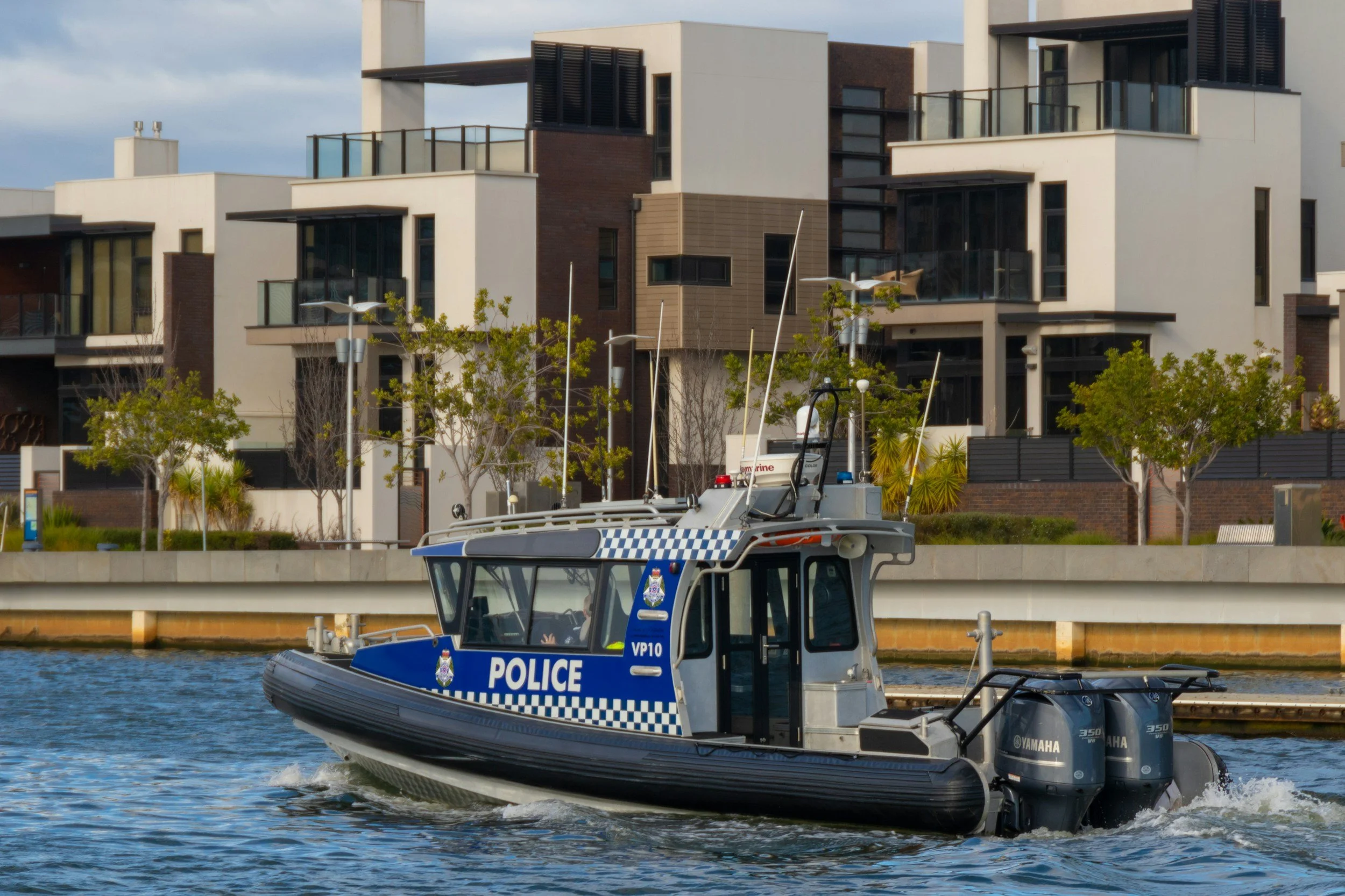 A police boat on a waterway with modern residential buildings and trees in the background.