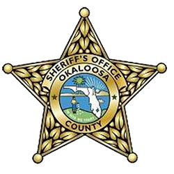 Seal of the Okaloosa County Sheriff's Office featuring a star with a centered emblem of a seagull, water, and trees, surrounded by a yellow band with black text.