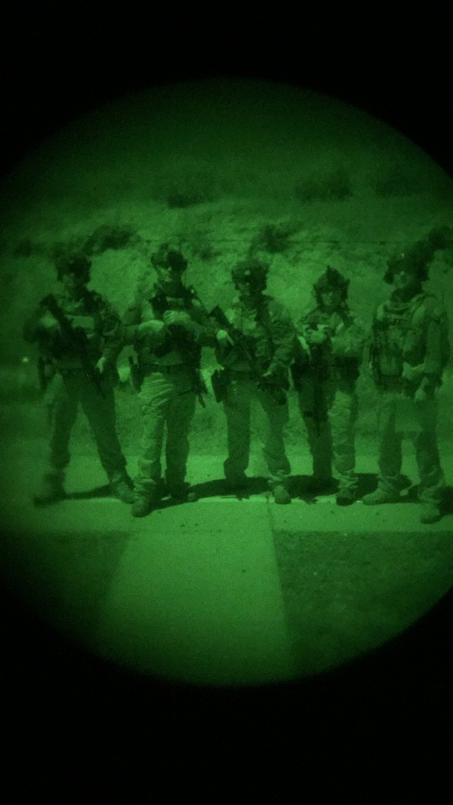 Group of soldiers standing outdoors during night, viewed through night vision goggles with a green hue.