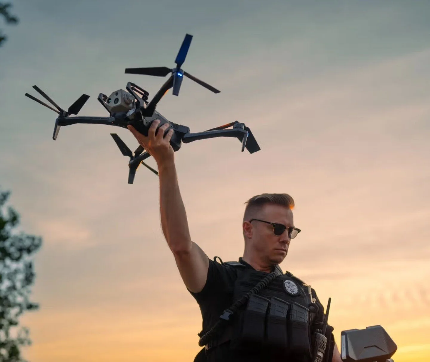 A police officer holding a drone against a sunset sky.
