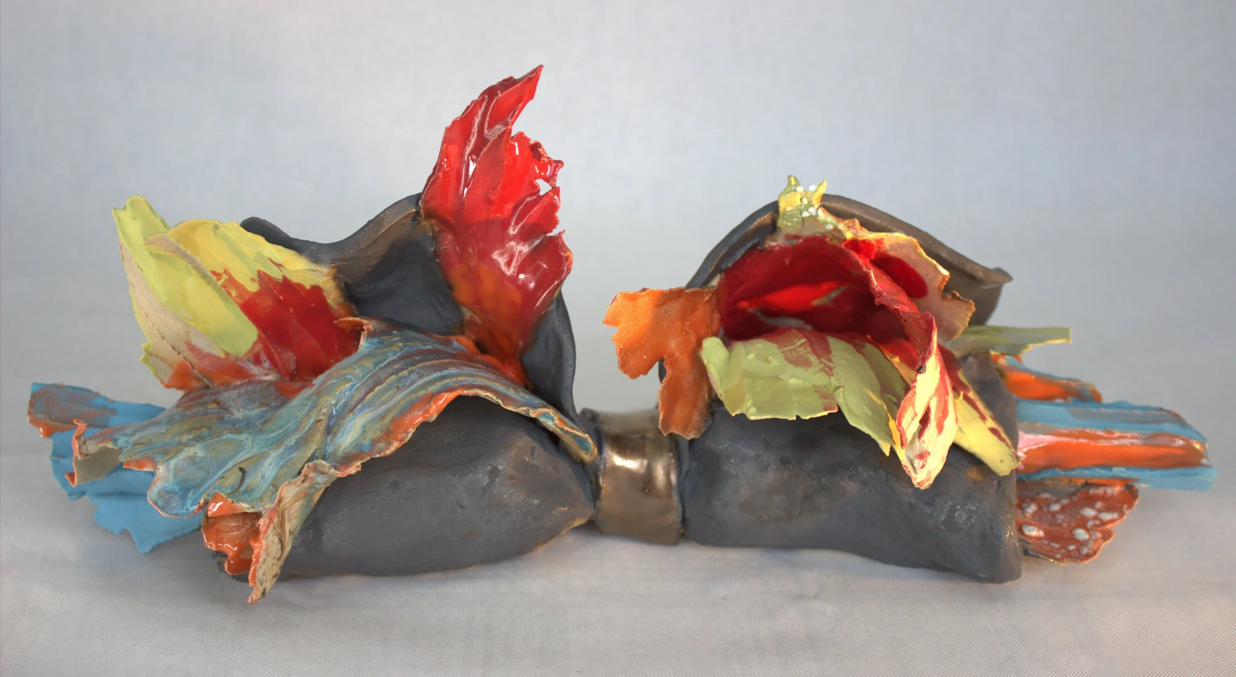 Colorful abstract ceramic sculpture with red, yellow, green, blue, and orange elements resembling wings or leaves.