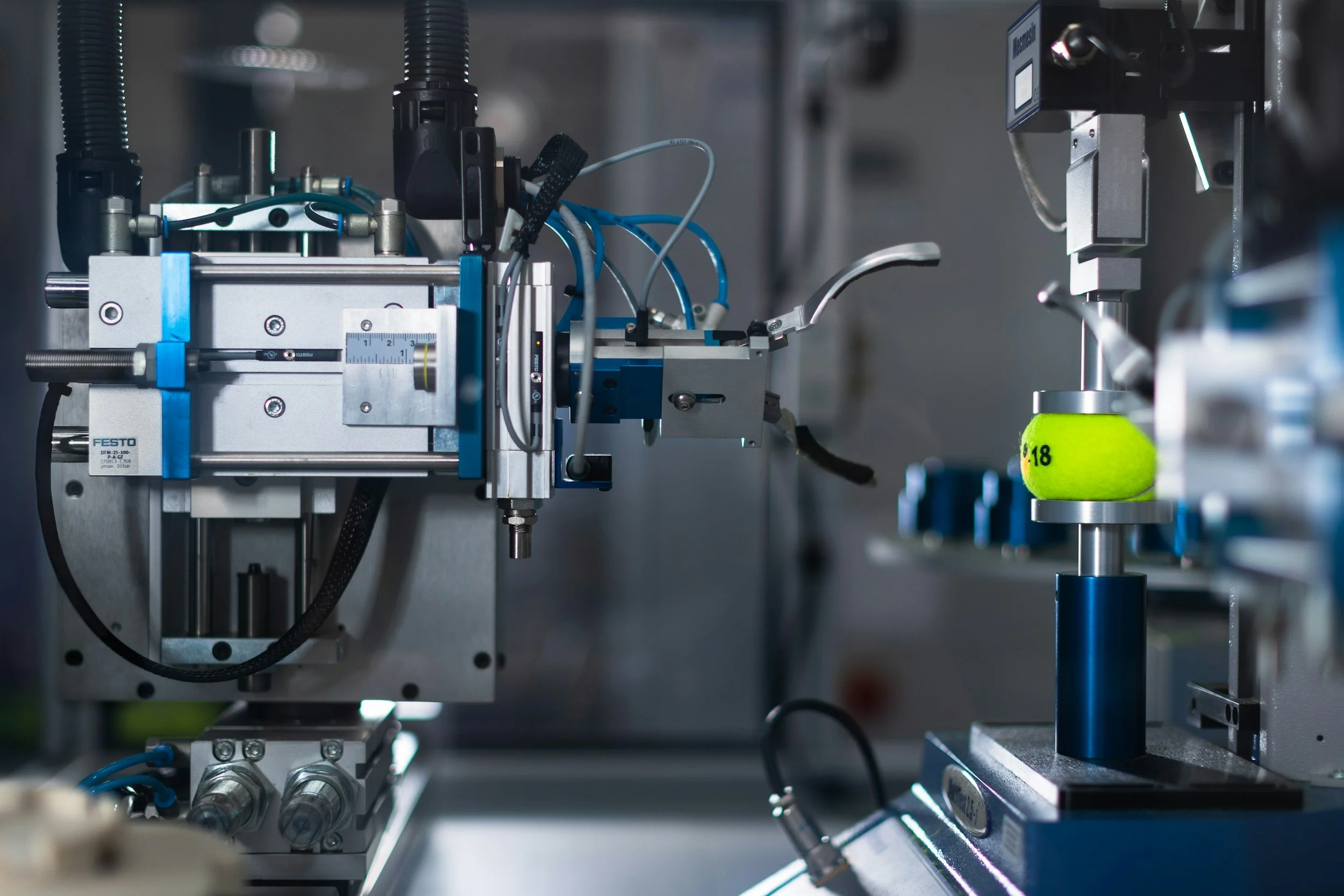 Close-up of a scientific machinery setup with metal components, sensors, and wires, including a green tennis ball marked with the number 18 on a steel platform.