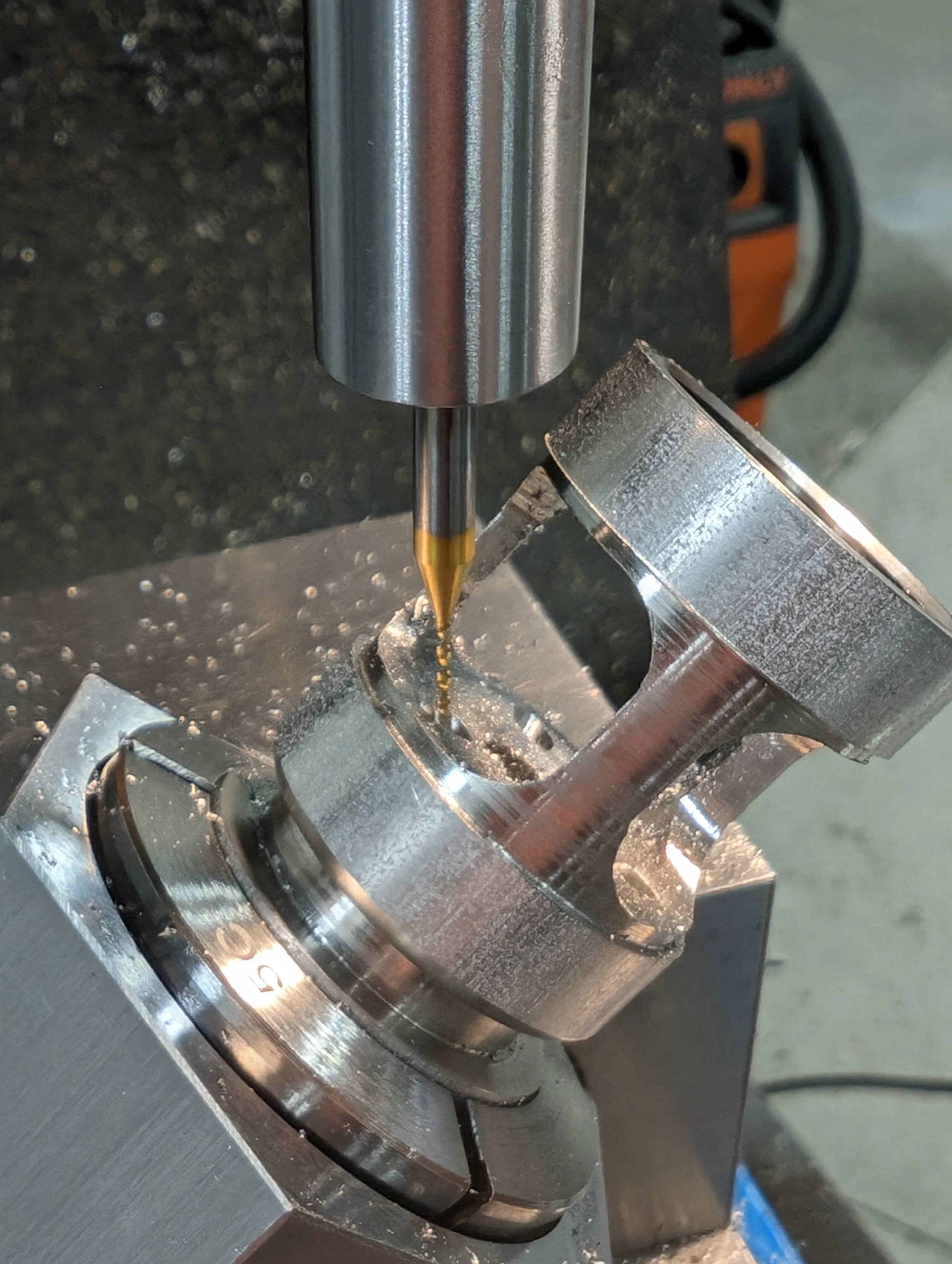 A precision machine tool with a drill bit aligned to drill into a metallic workpiece held in a chuck, with visible metallic shavings.