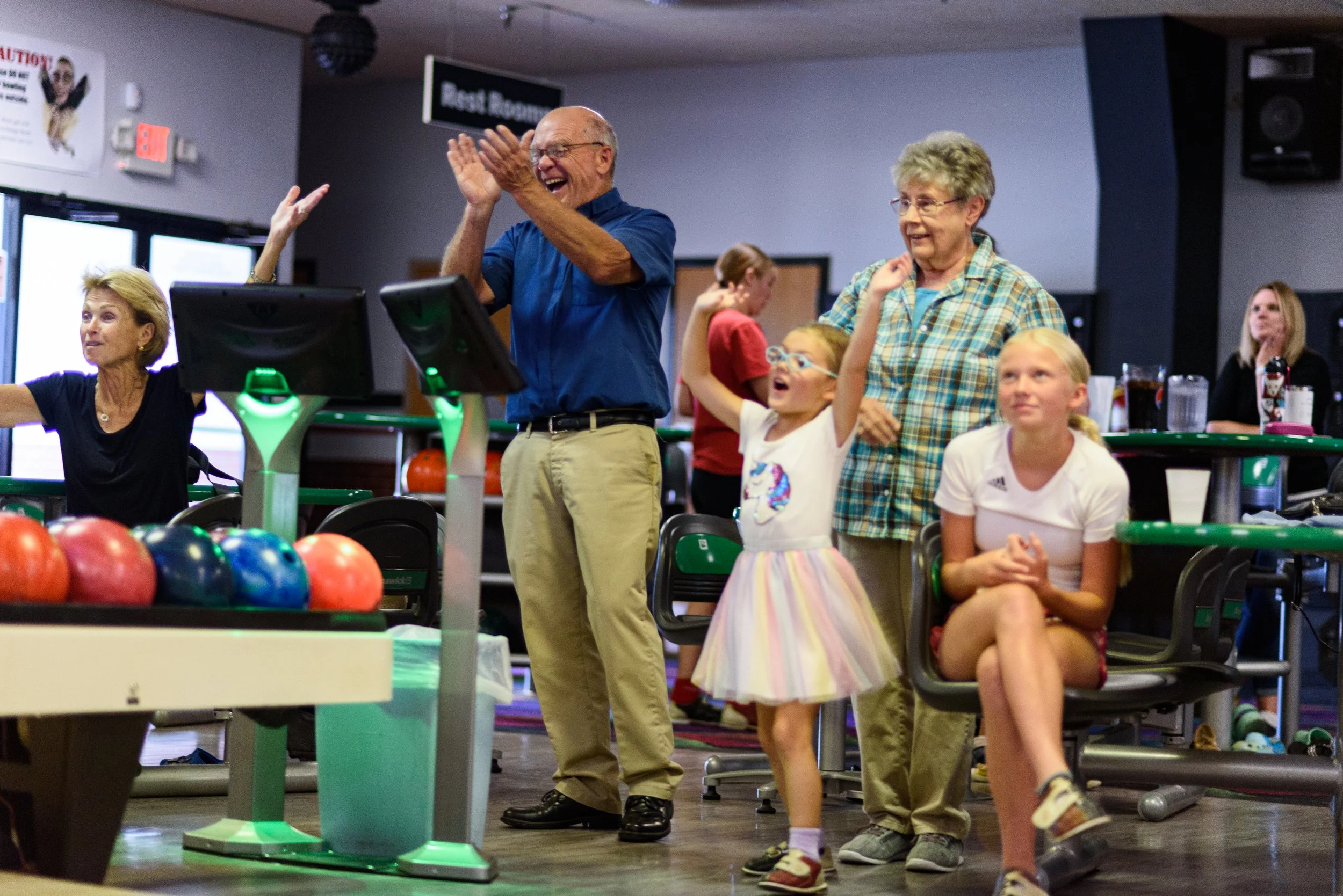 People enjoying themselves at a bowling alley, with bowling balls in the foreground and lanes in the background.