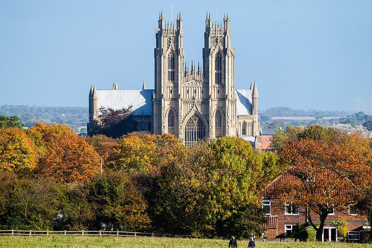 A large Gothic cathedral with twin towers, surrounded by autumn-colored trees, with a clear blue sky in the background.