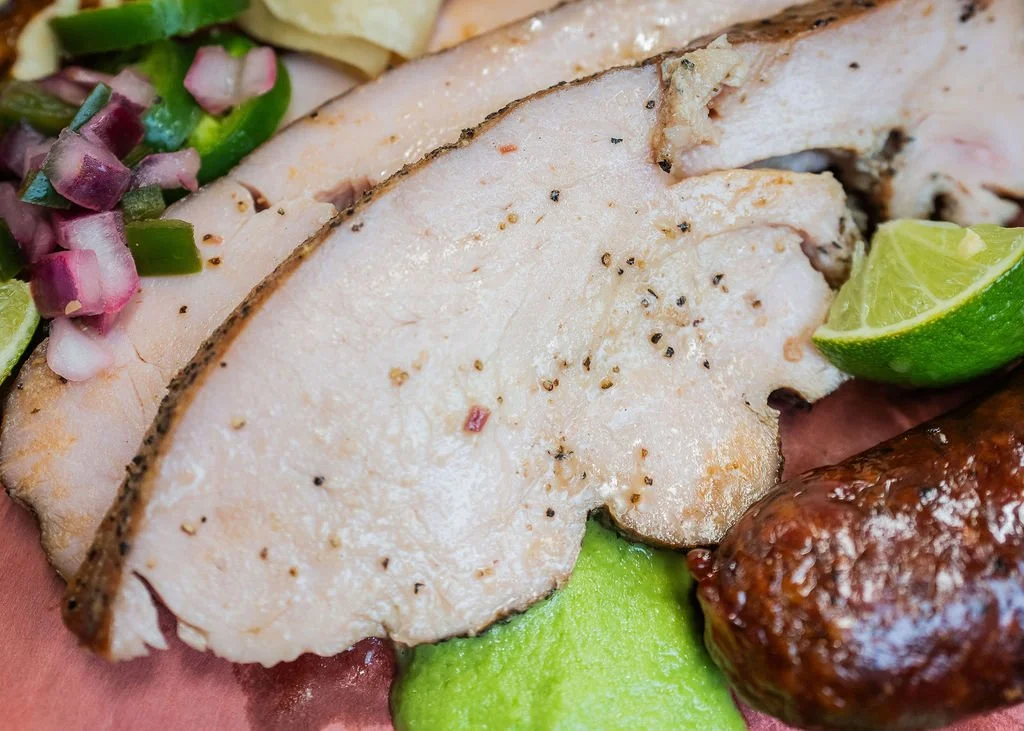 Close-up of sliced cooked turkey breast with black pepper, alongside a lime wedge, a meatball, and chopped green onions for garnish.