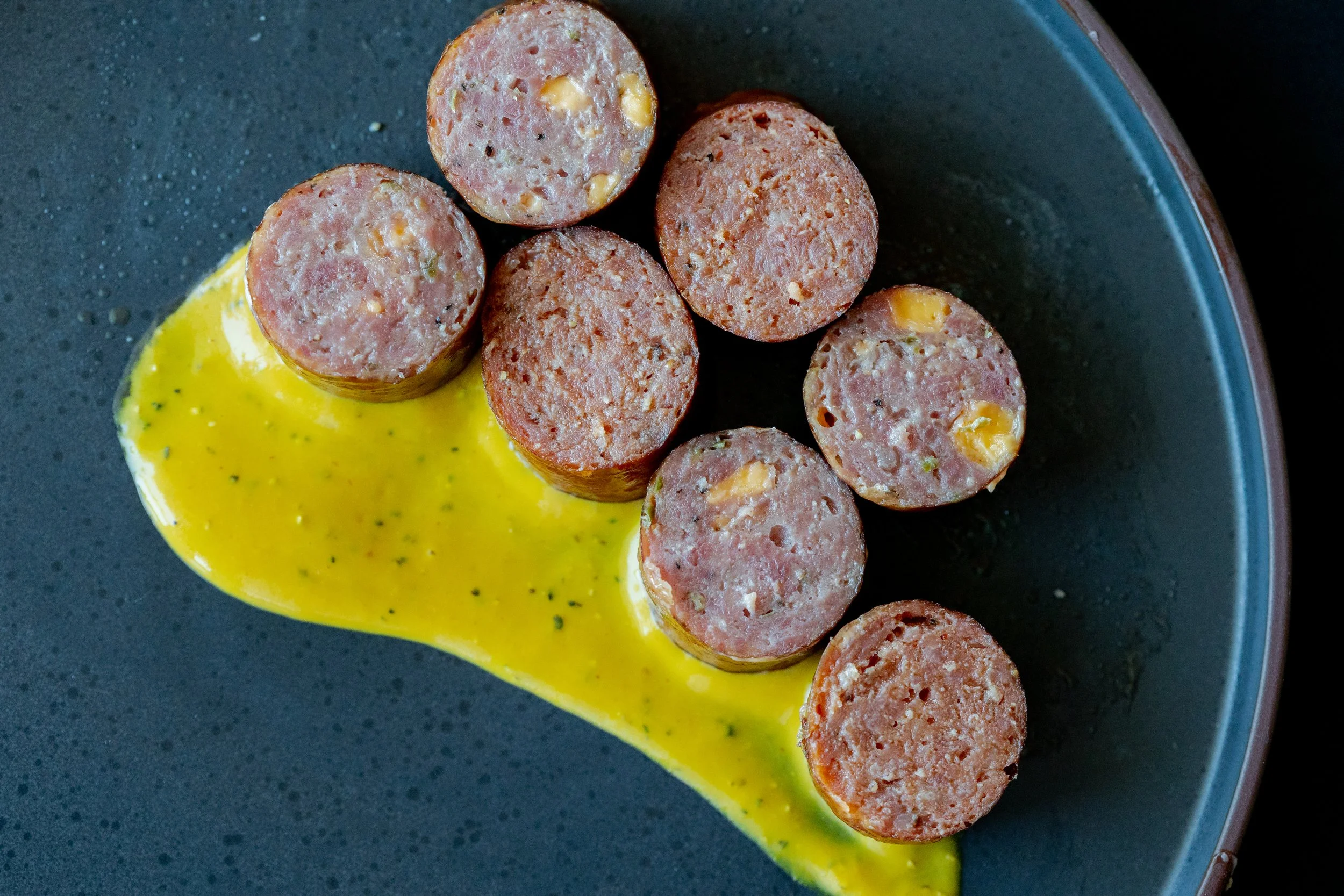 Slices of sausage on a black plate with a yellow sauce.