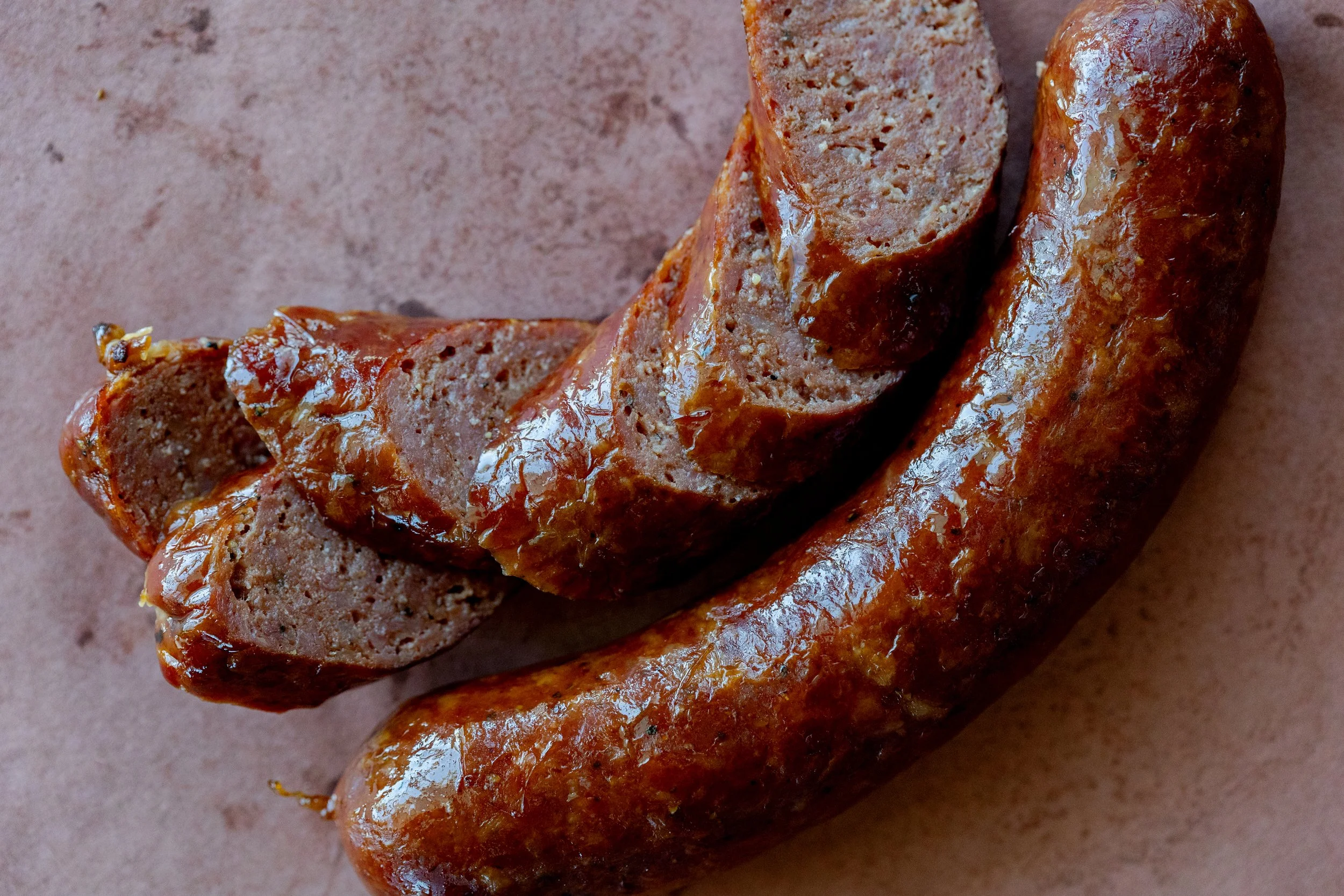 Close-up of cooked sausage links on a brown surface, with one sausage cut open to reveal the ground meat inside.
