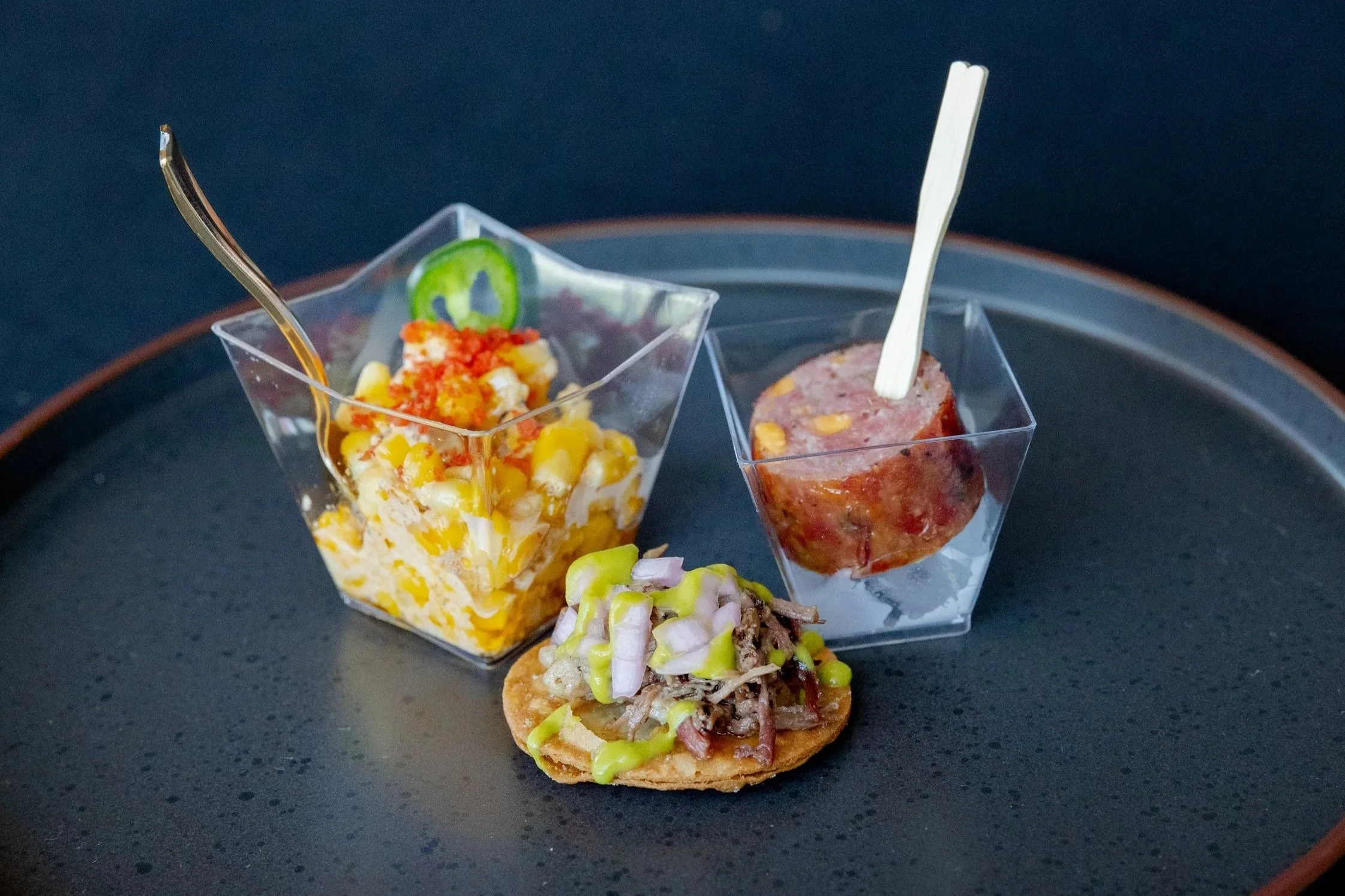 Three small glasses filled with different types of appetizers on a black surface.