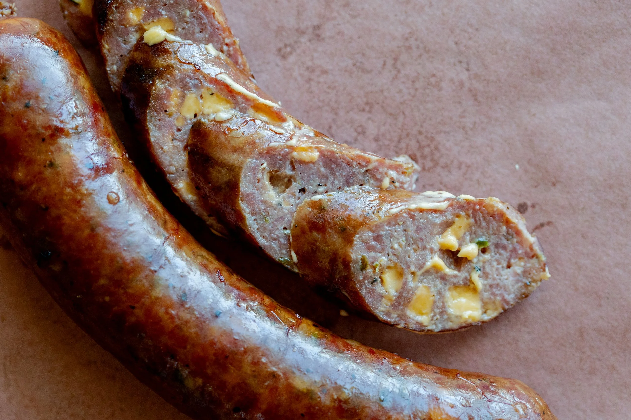 Close-up of a cooked sausage link, cut open to reveal the ground meat and cheese filling inside.
